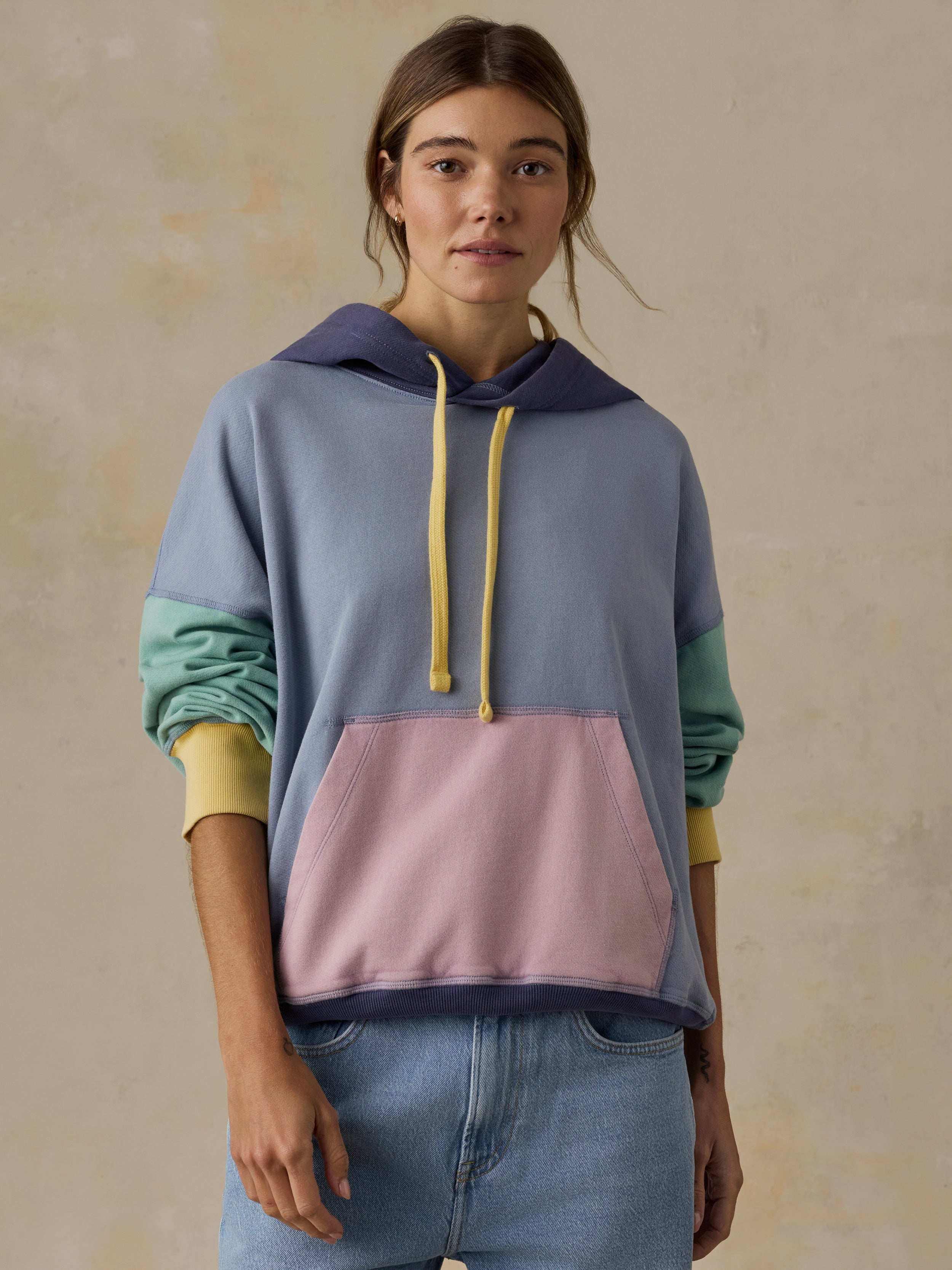 Woman wearing colorblocked hoodie and blue jeans against a beige background