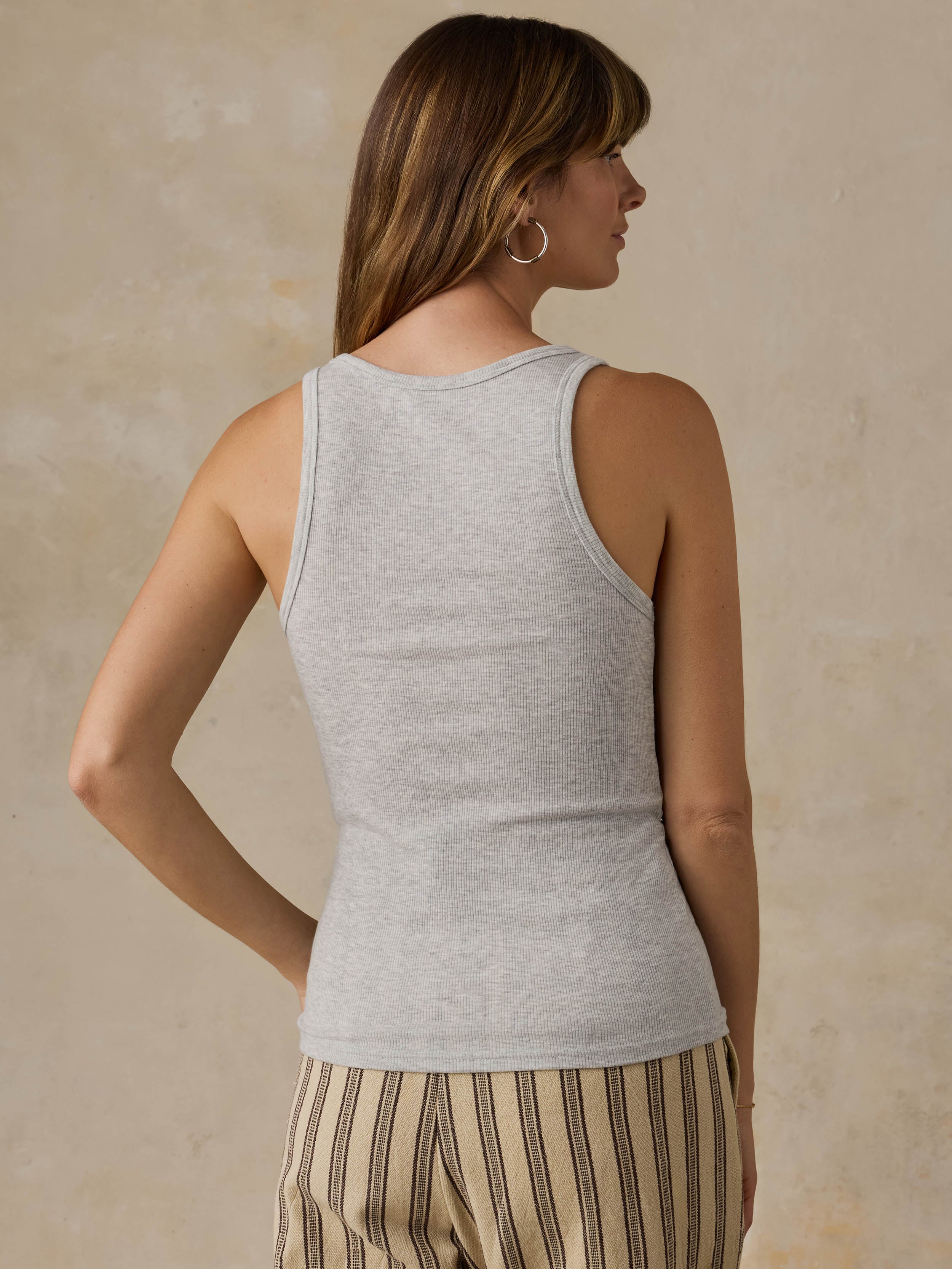 Woman wearing a grey tank top and striped pants against a beige background