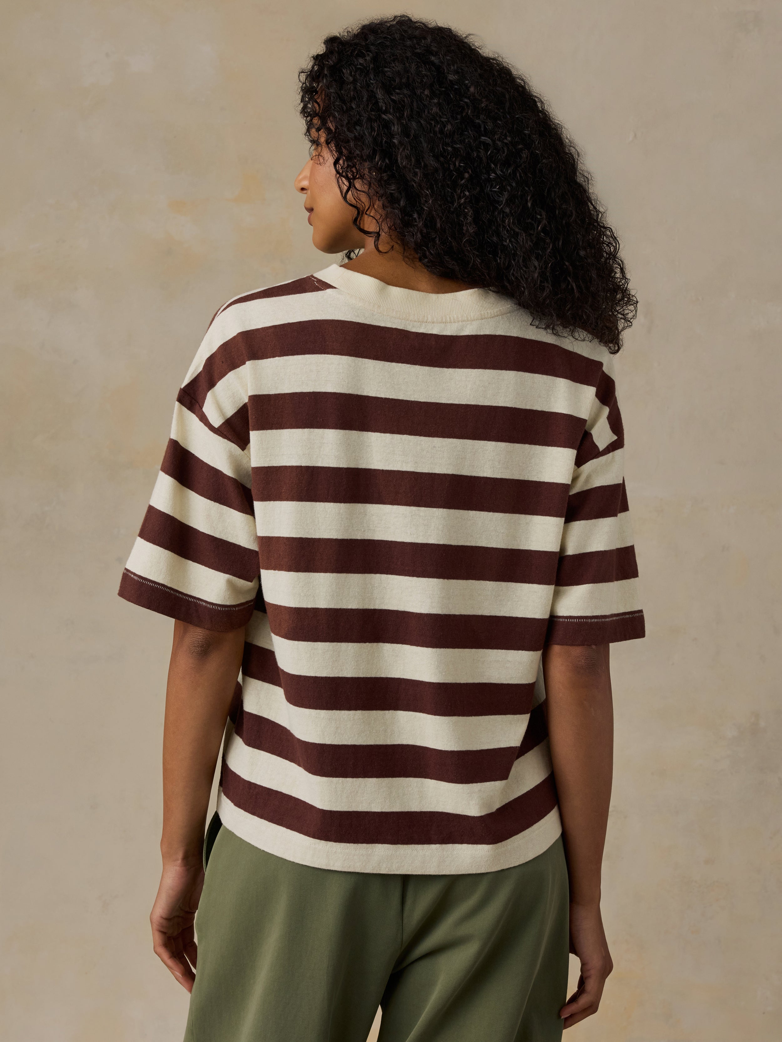Woman wearing a brown and white striped shirt with green pants against a beige background