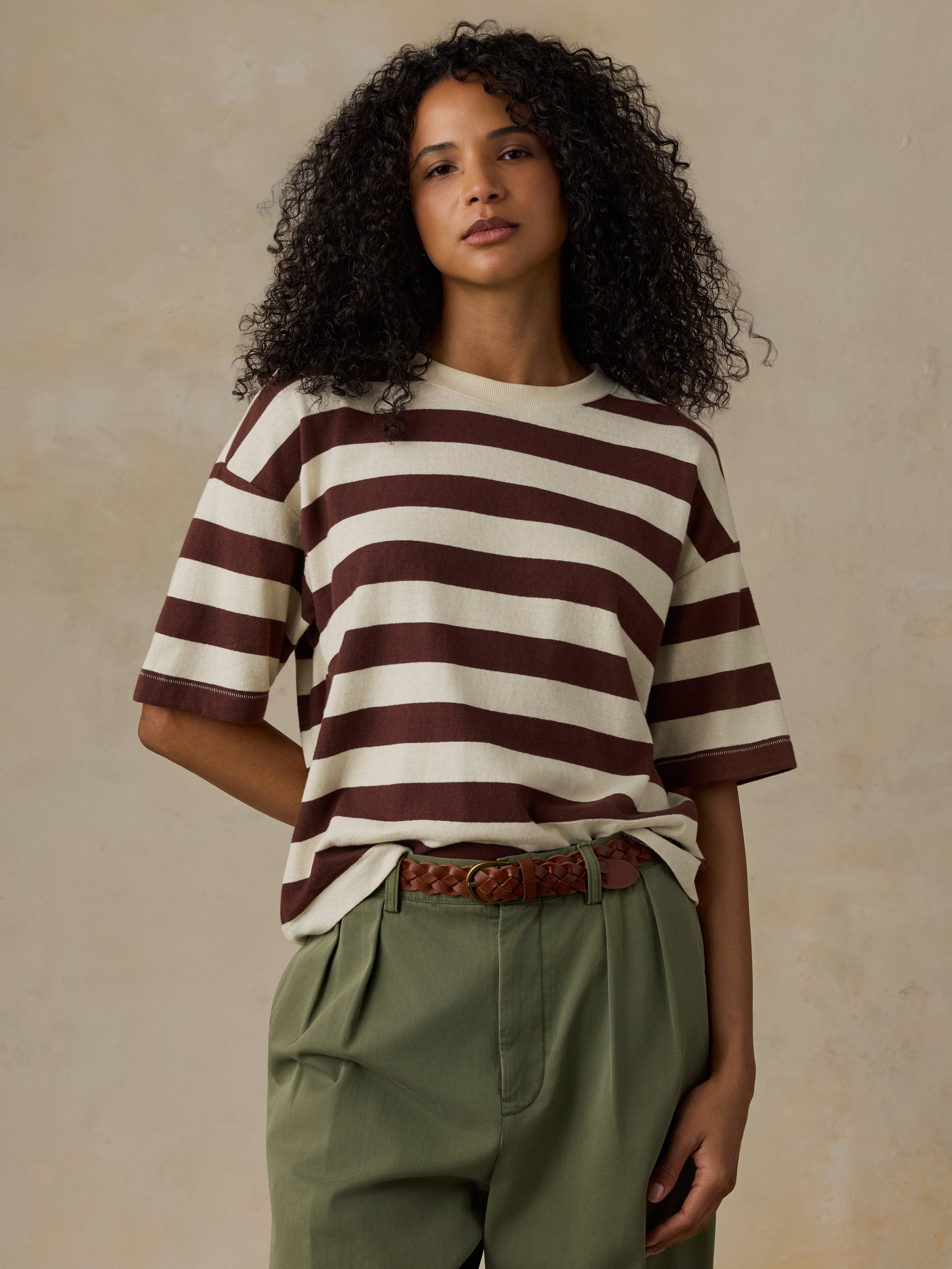 Woman wearing a brown and white striped shirt with green pants against a beige background