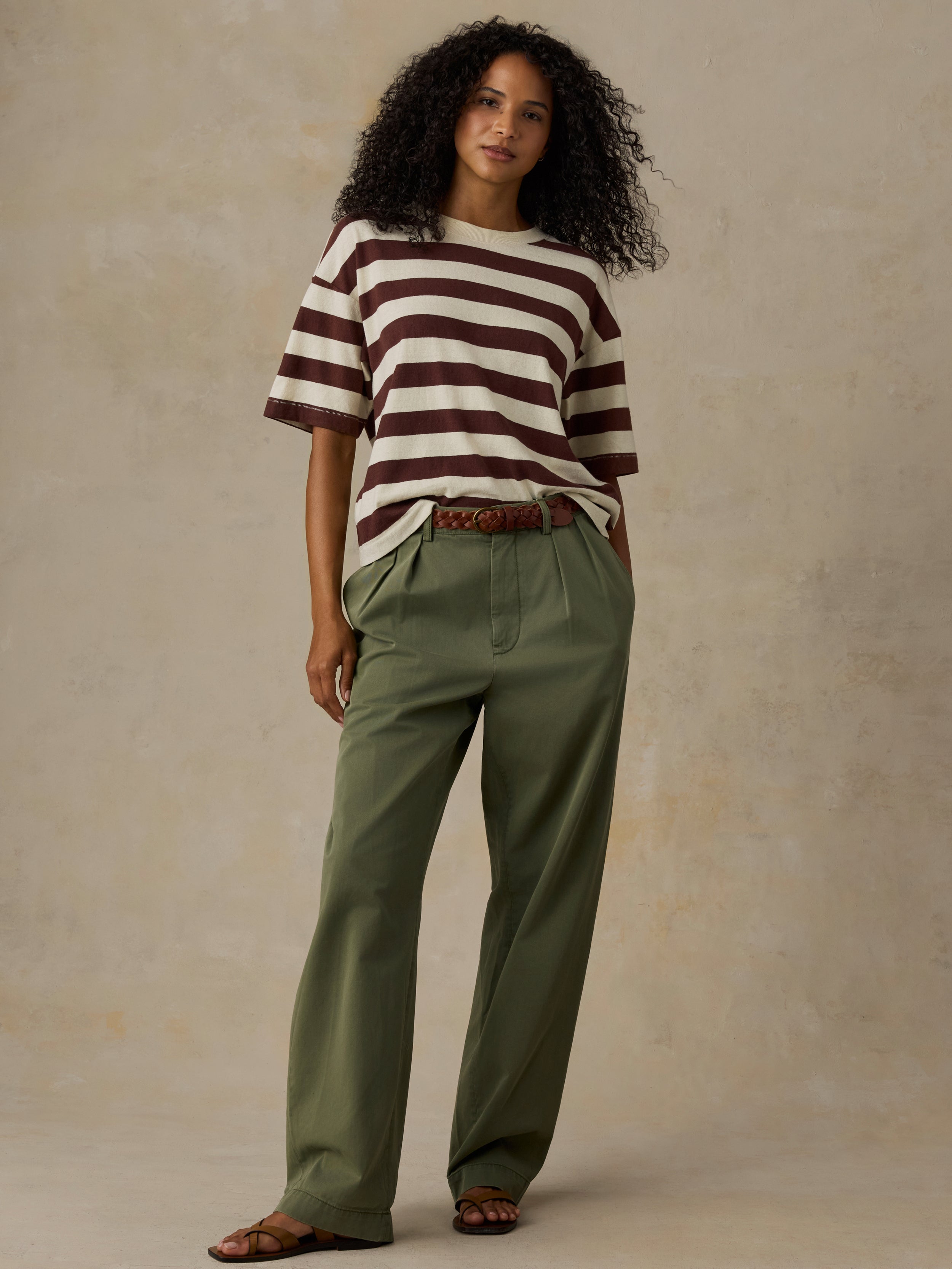 Woman wearing a brown and white striped shirt with green pants against a beige background