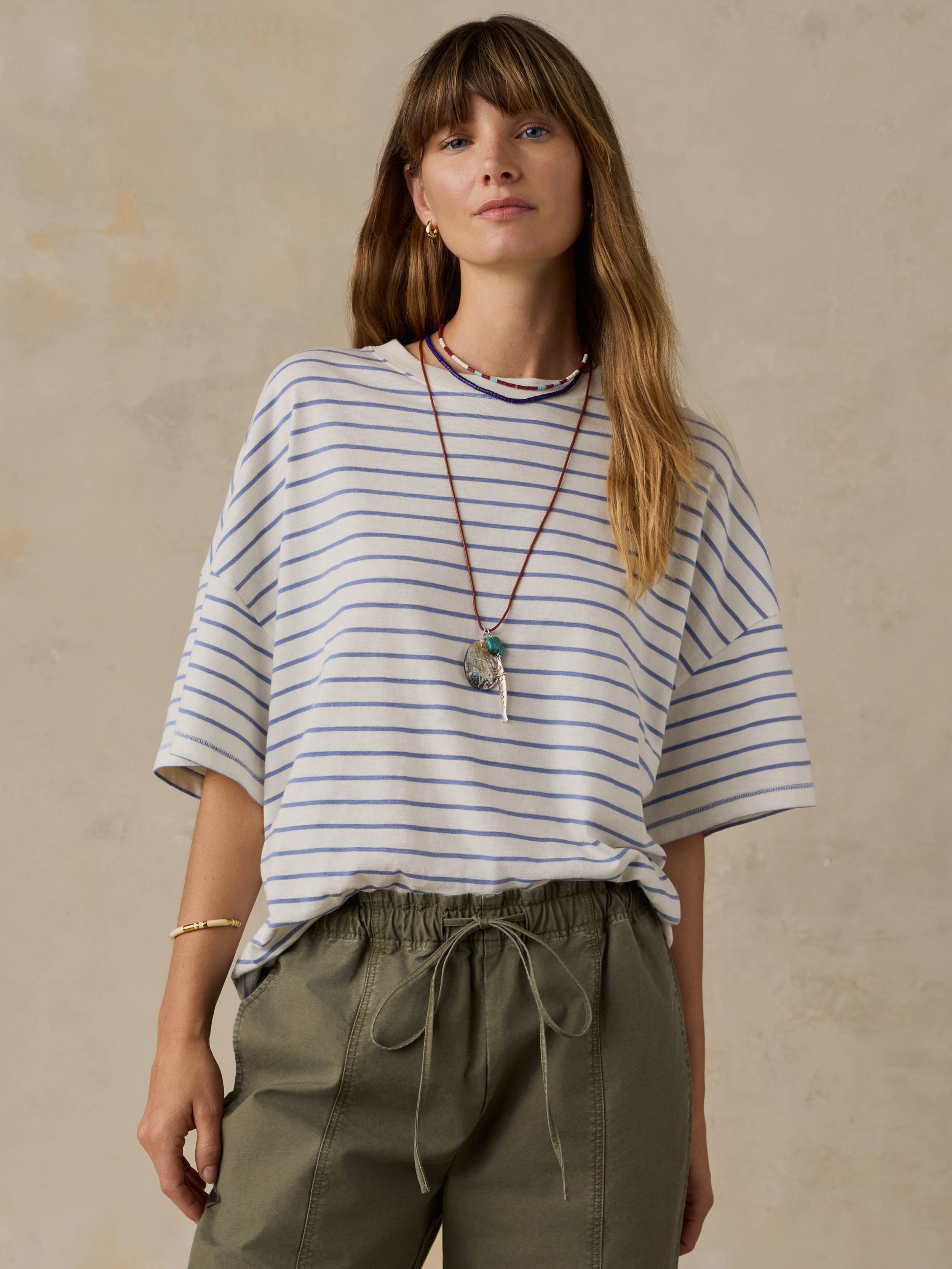 Woman wearing blue and white striped t-shirt and green pants against a beige background