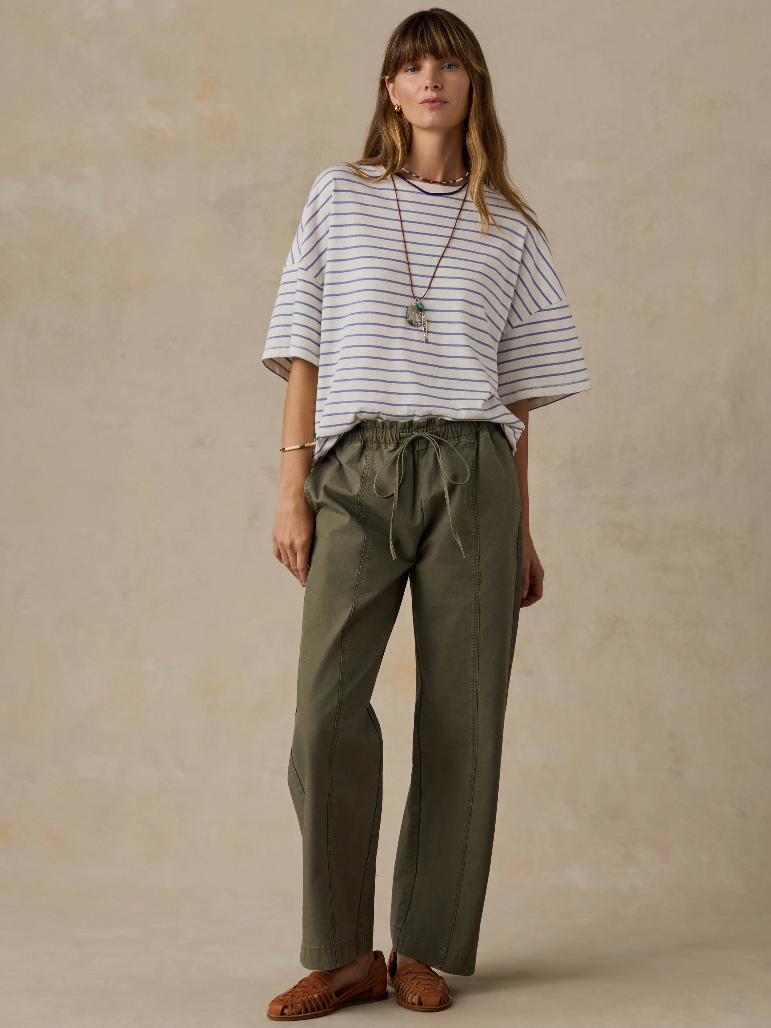 Woman wearing blue and white striped t-shirt and green pants against a beige background