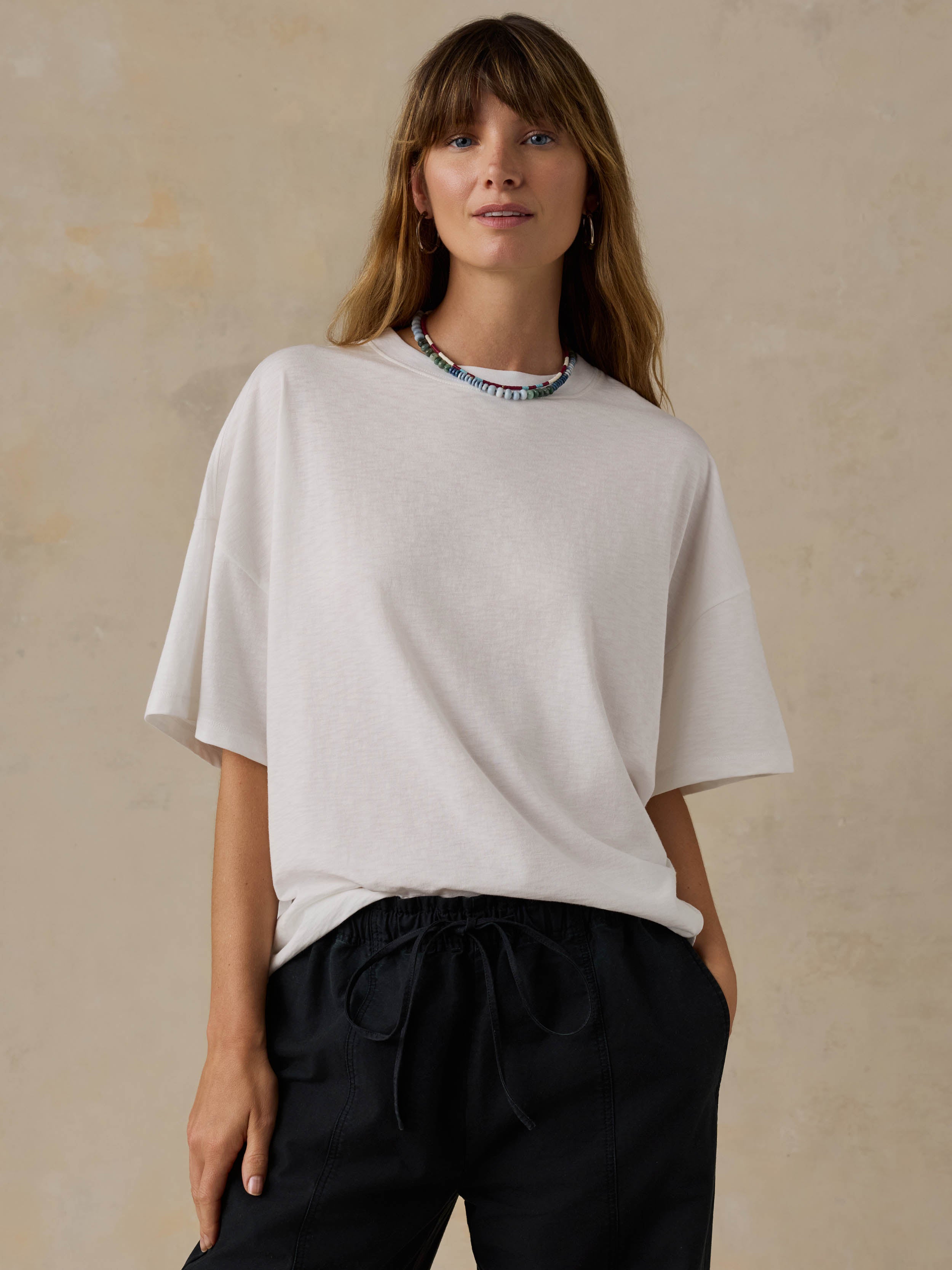Woman wearing a white t-shirt and black pants against a beige background