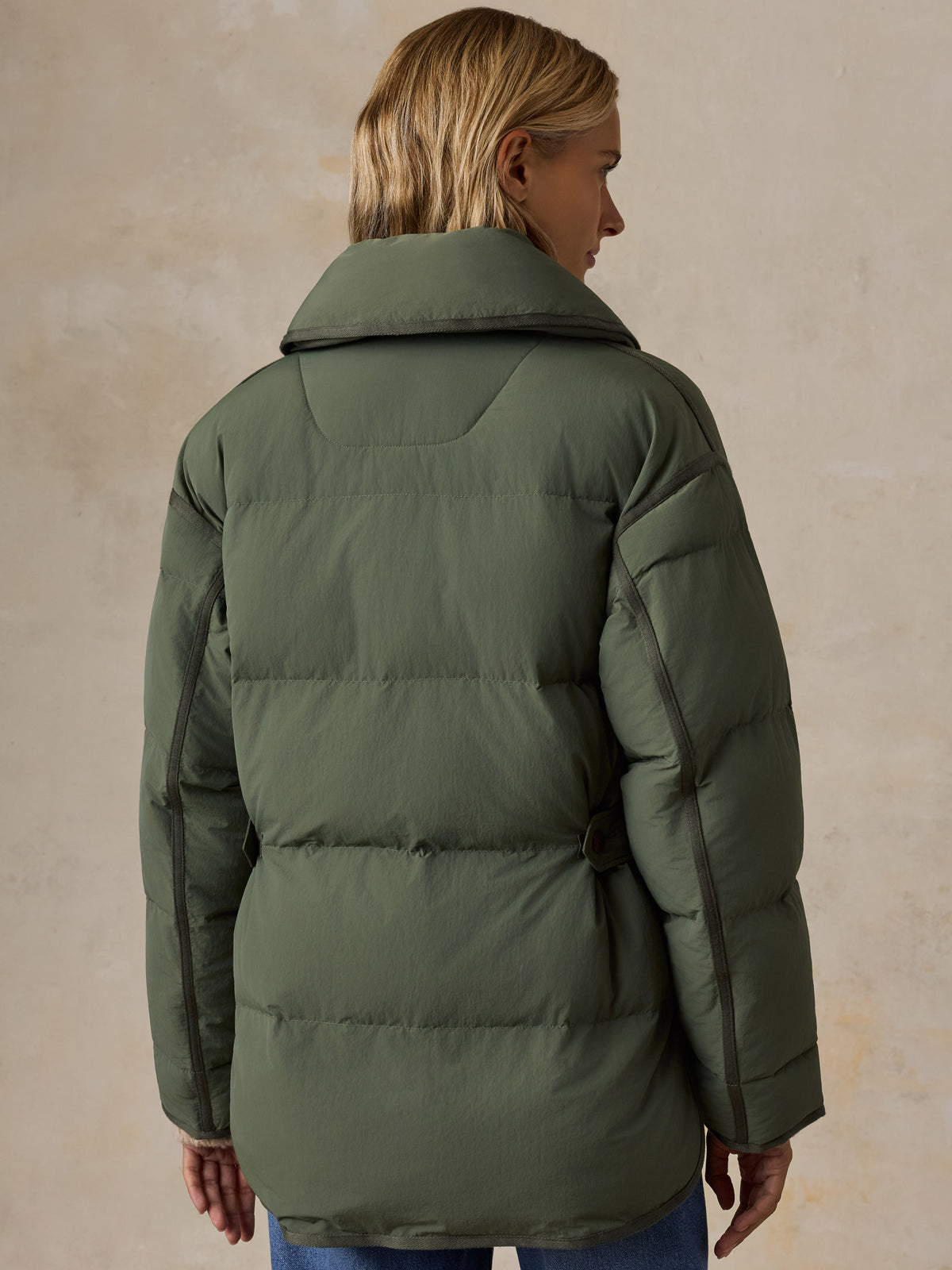 A woman viewed from the back wearing a green jacket and blue jeans, image 4 of 8