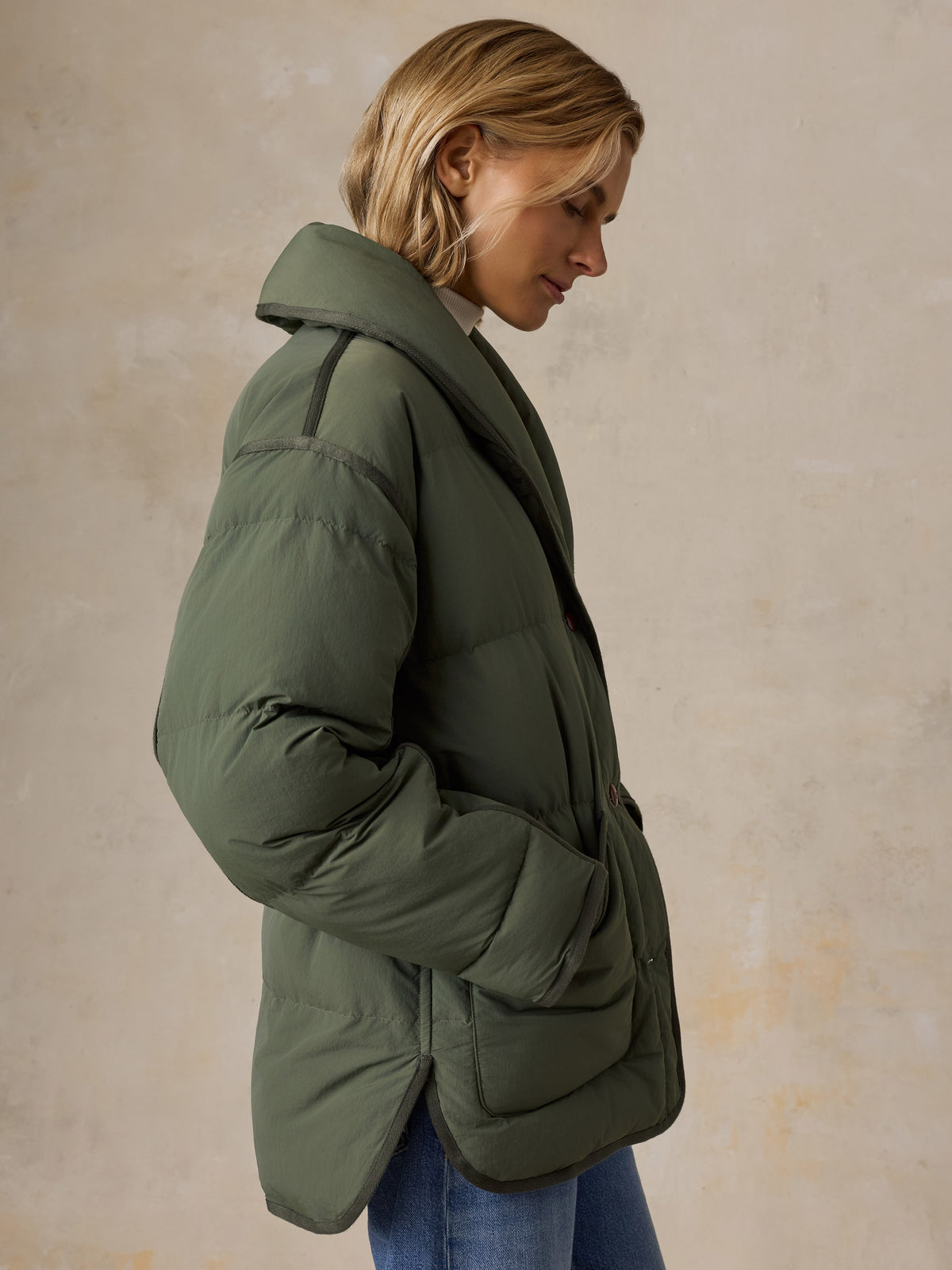 A woman wearing a green jacket and blue jeans, image 8 of 8