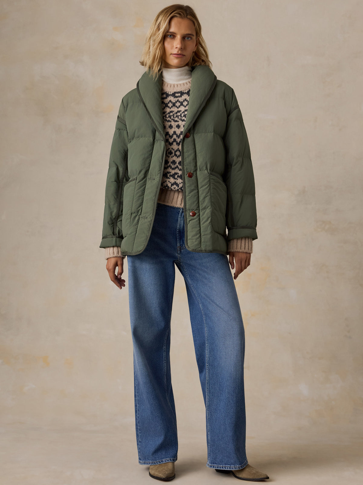 A woman wearing a green jacket over a knit sweater and blue jeans, image 2 of 8