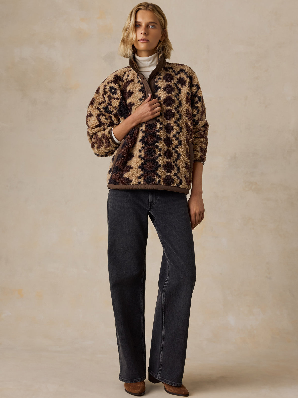 A woman wearing a brown printed fleece jacket, black jeans, and brown boots, image 2 of 5