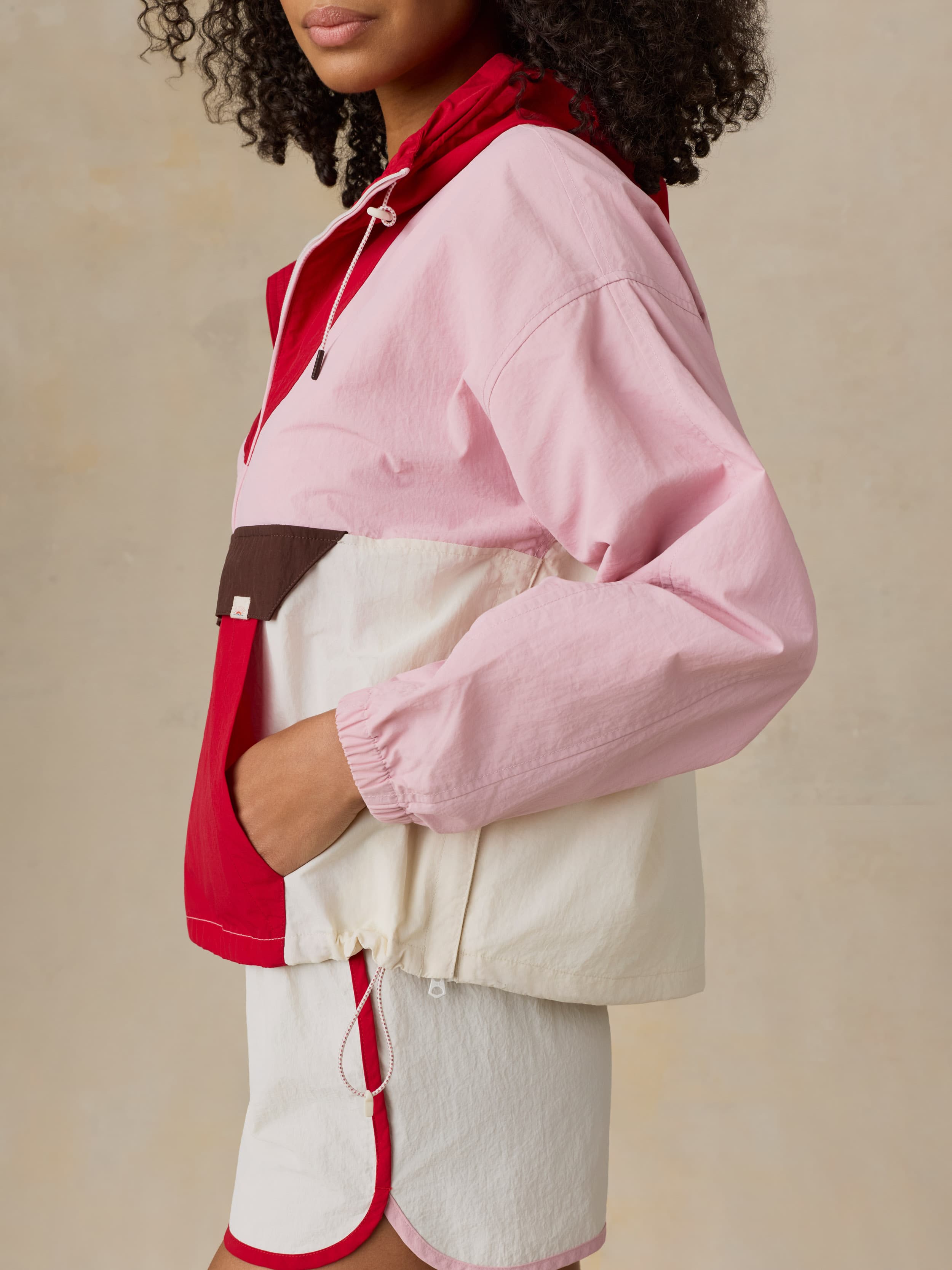 Woman wearing a pink and red jacket with white pants on a beige background