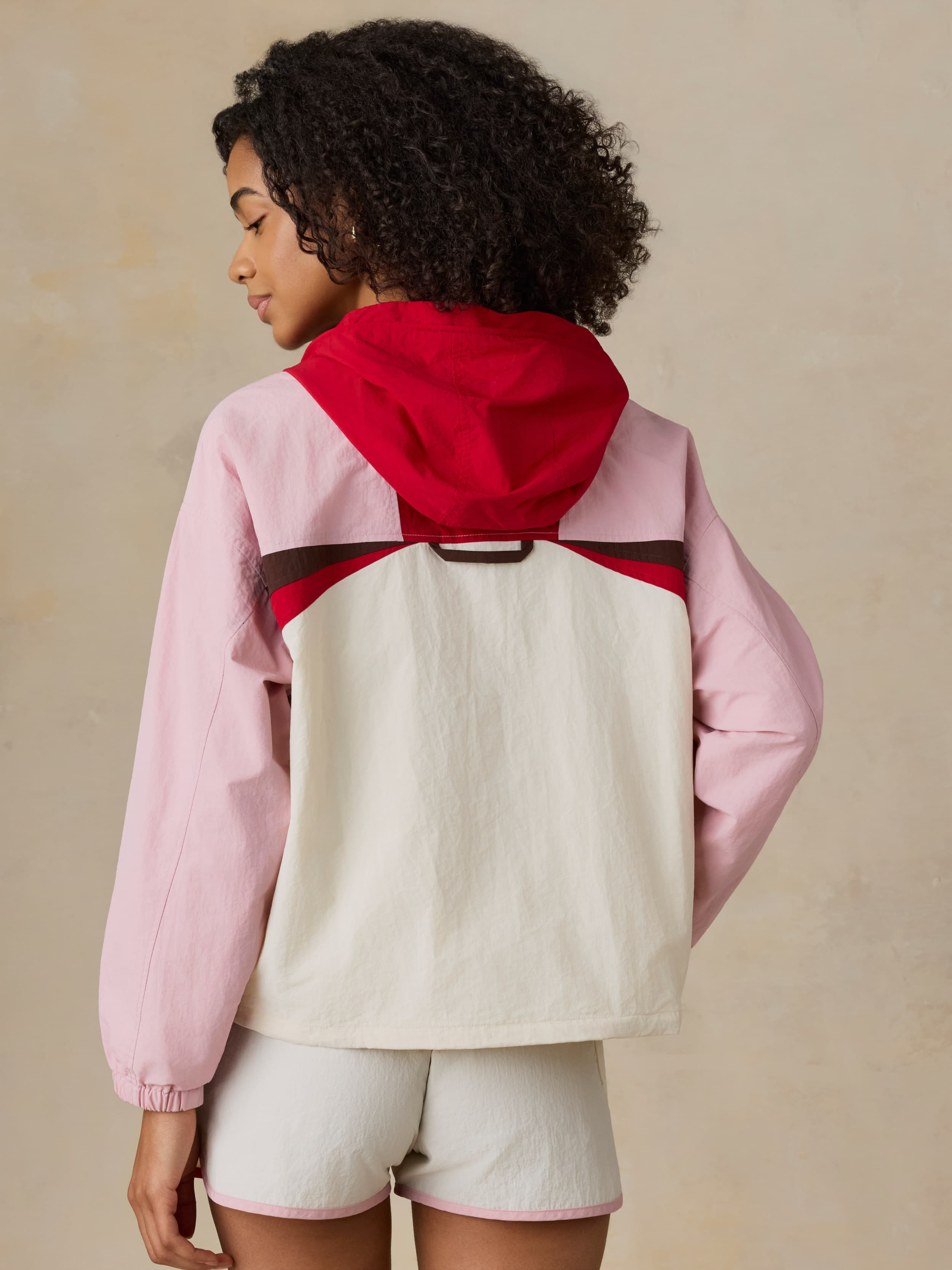 Woman wearing a colorful jacket with pink, red, and beige sections on a beige background
