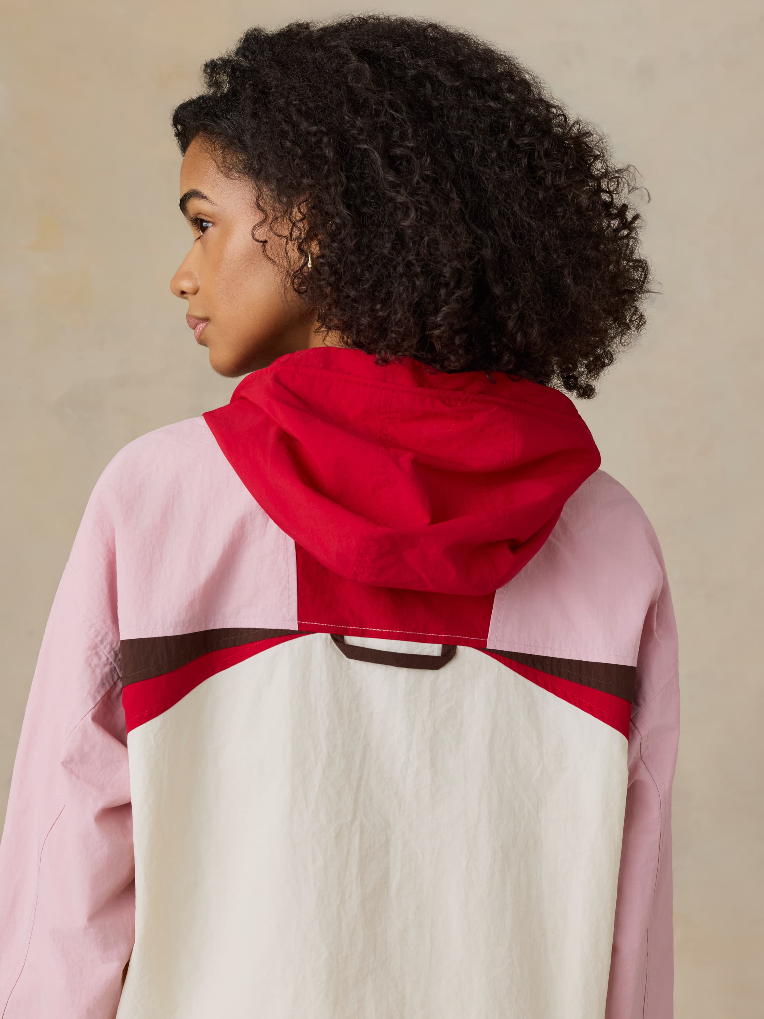 Woman wearing a pink and red jacket with white pants on a beige background
