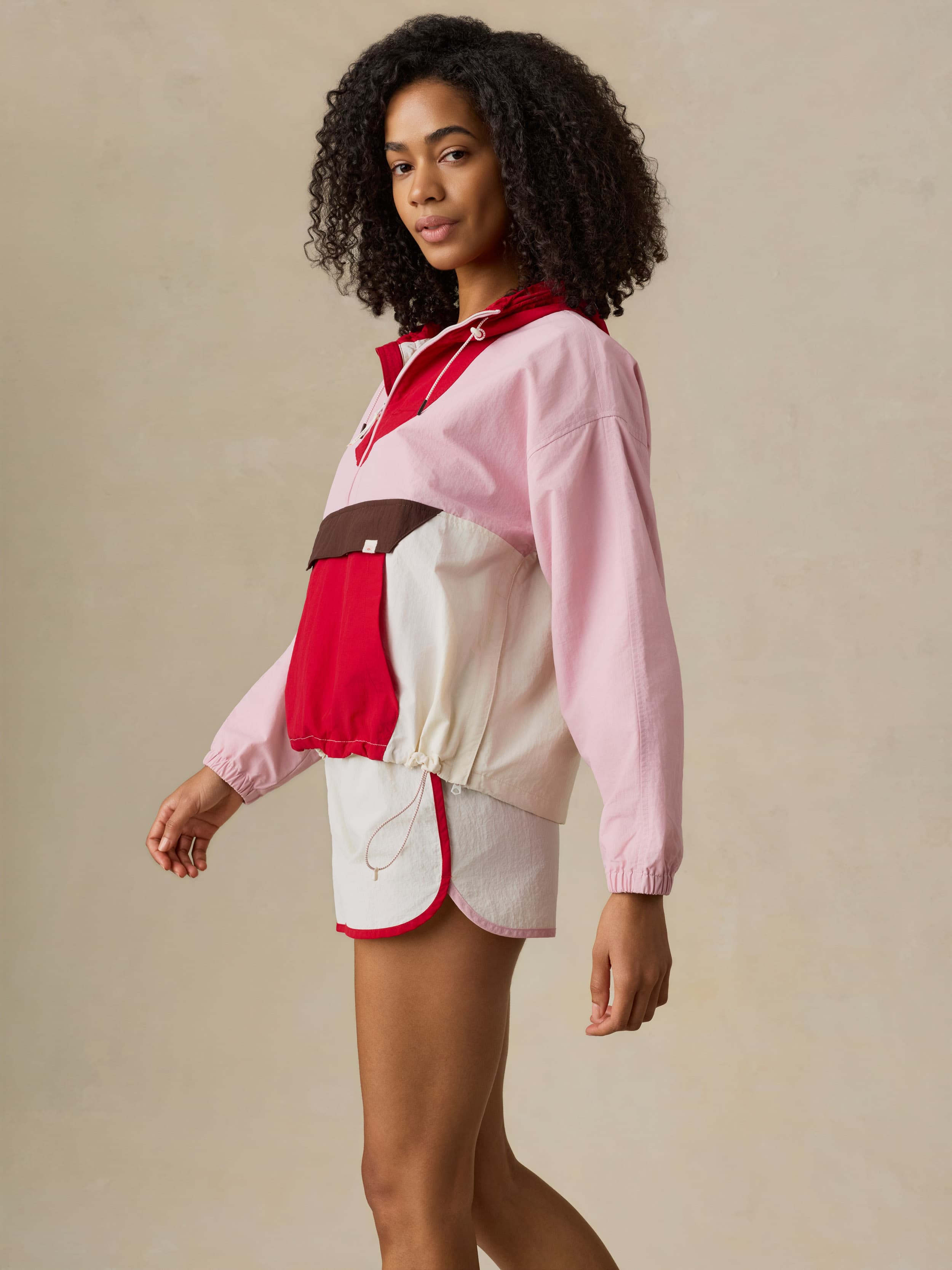 Woman wearing a pink and red jacket with white pants on a beige background