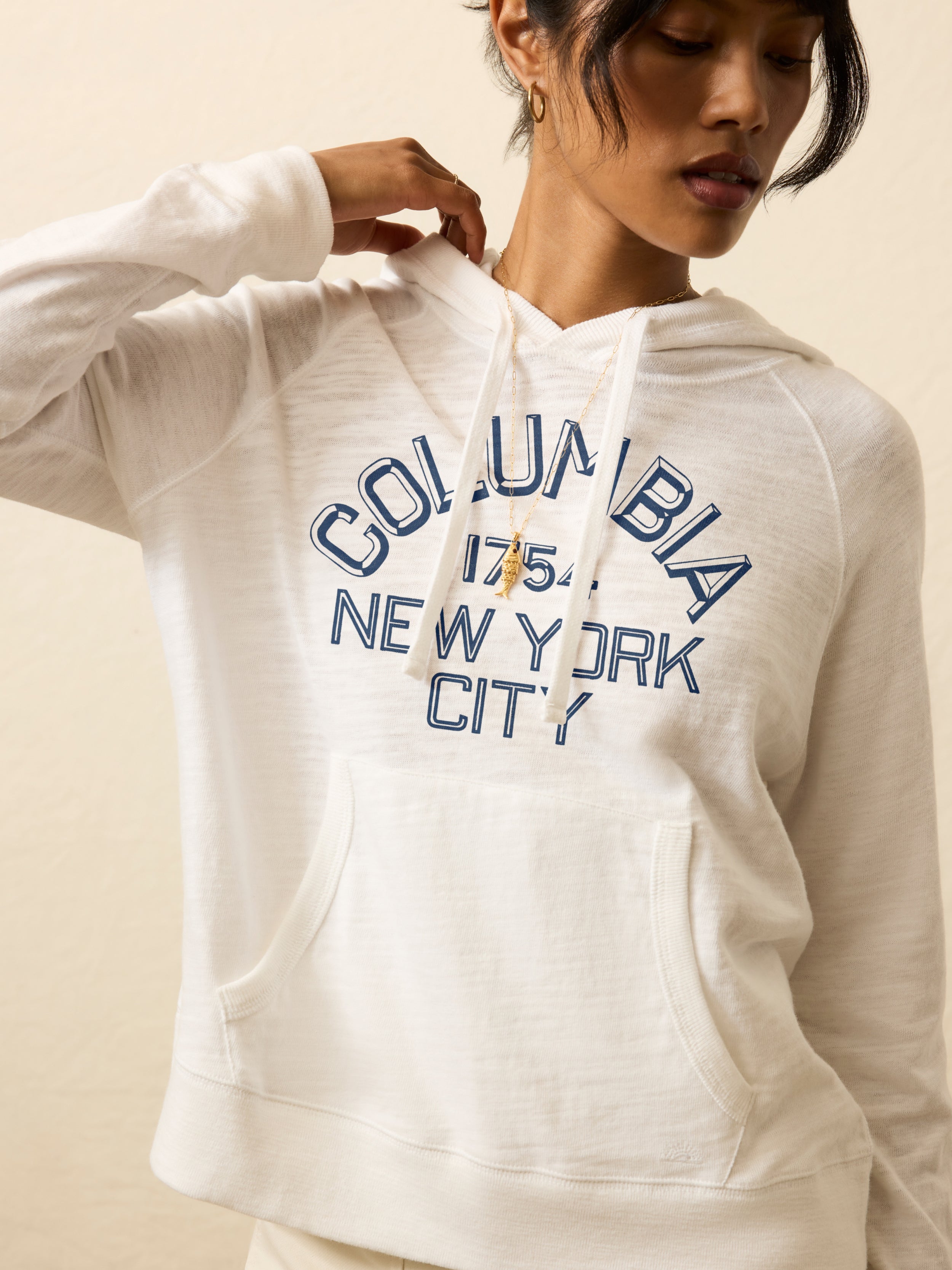 Woman wearing an ivory heather hoodie with Columbia University graphic at the center chest against a beige background