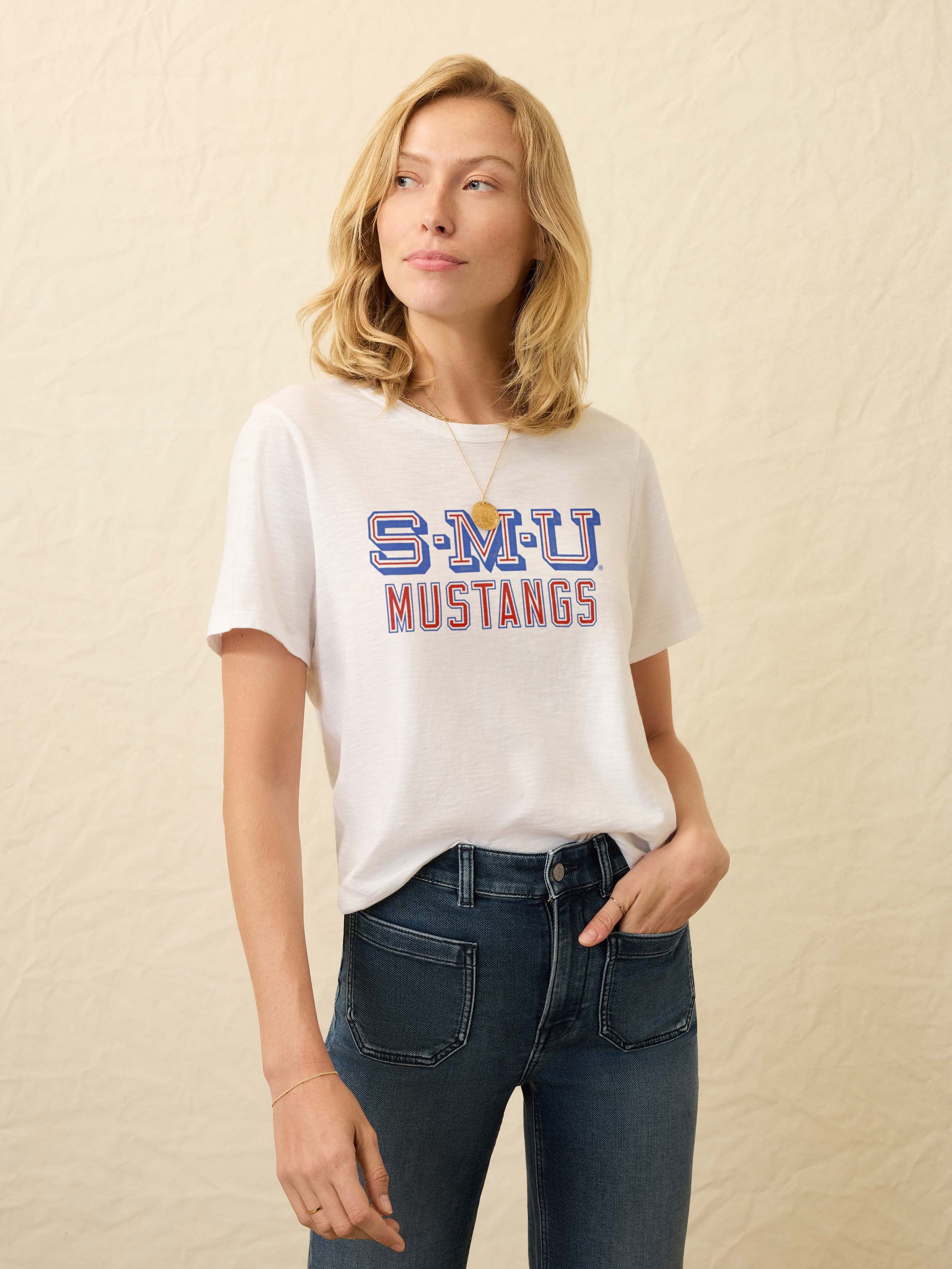Woman wearing a white t-shirt with SMU graphic on the chest against a beige background