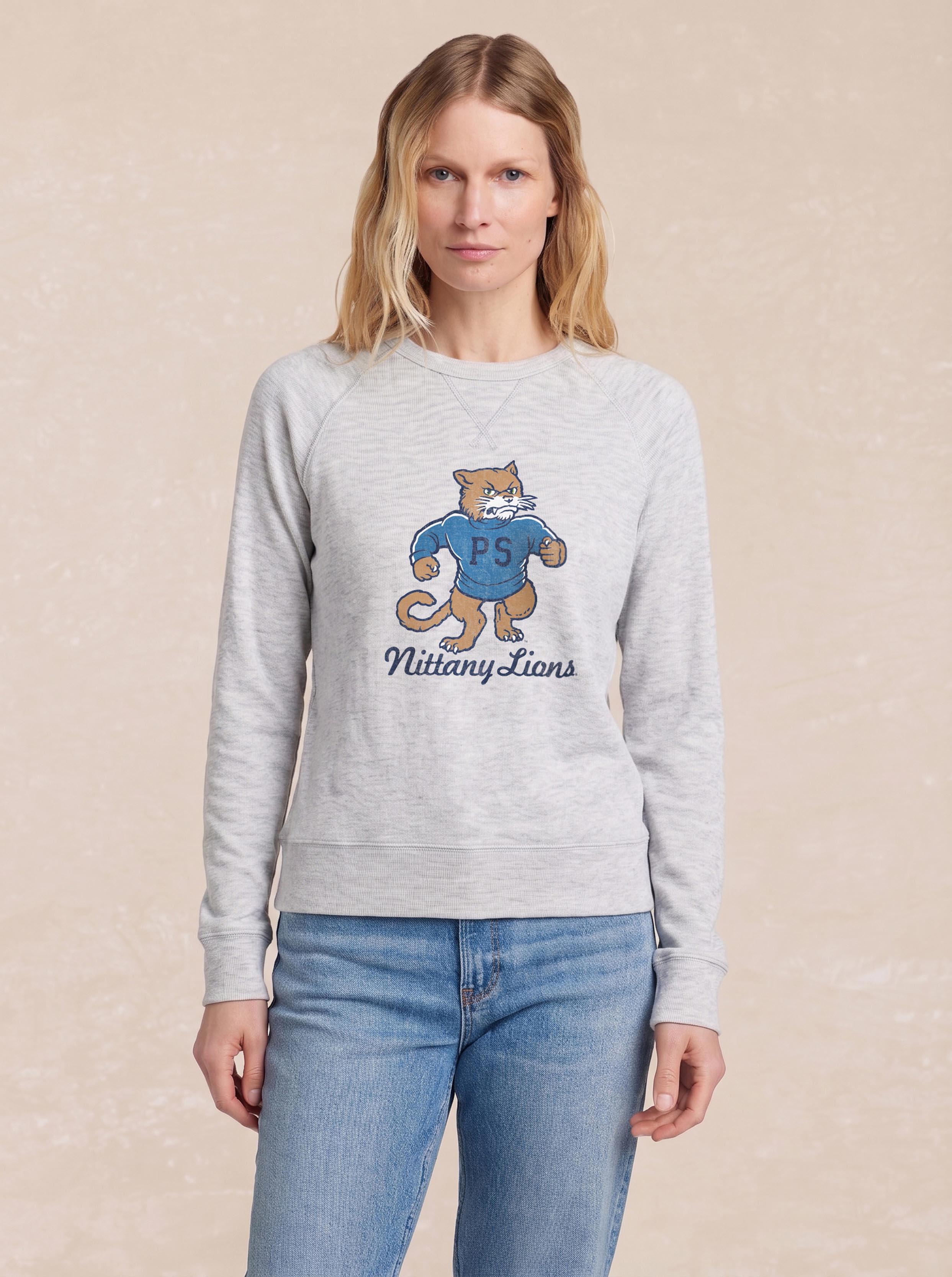 A woman wearing a grey Penn State graphic crewneck and blue jeans