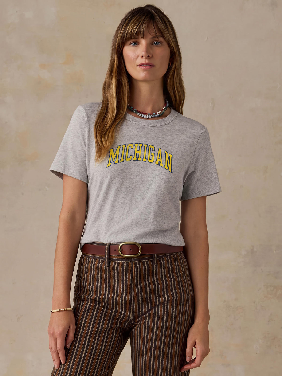 A woman wearing a grey University of Michigan tee and brown striped pants, image 1 of 1