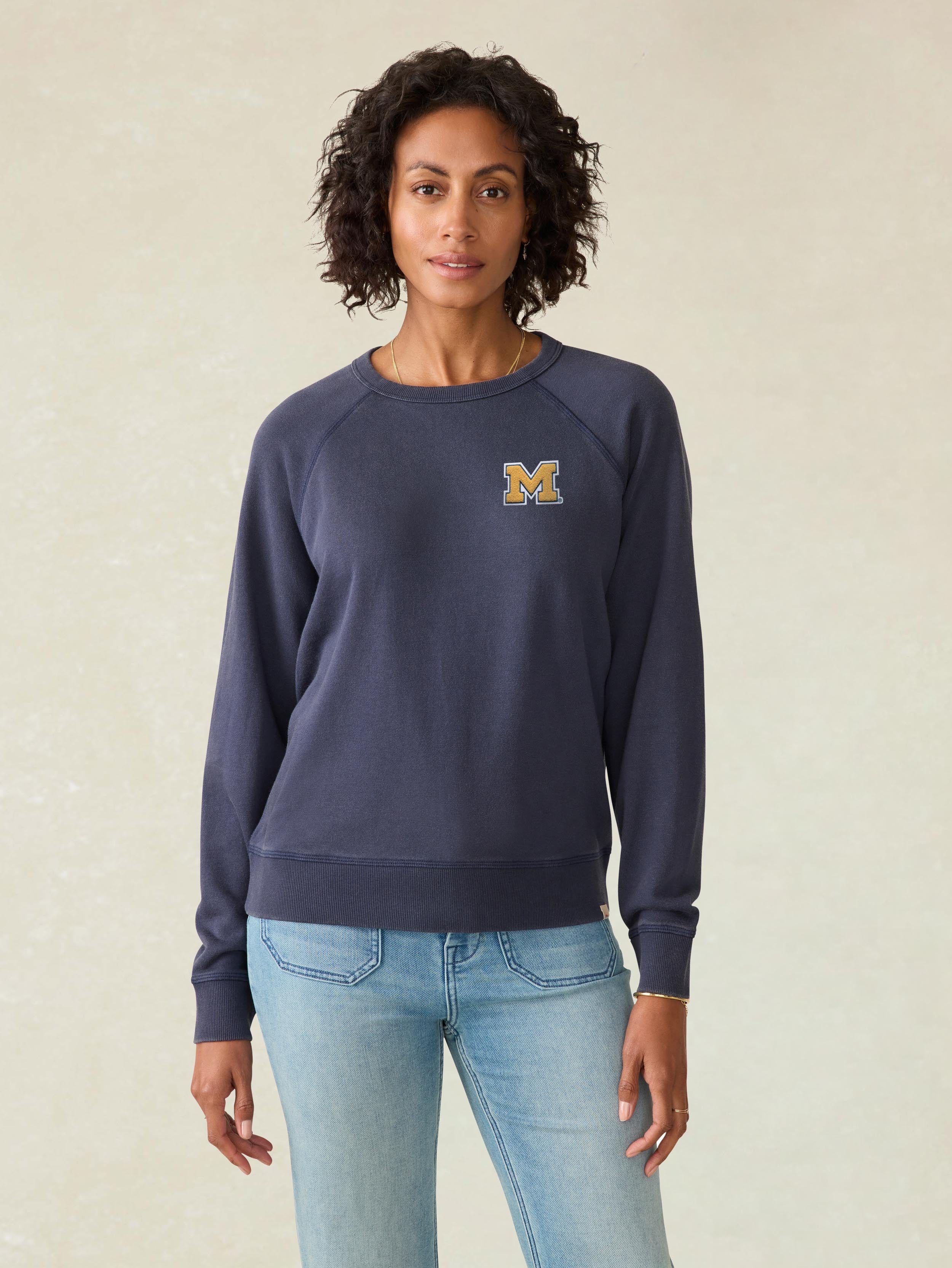 A woman wearing a blue University of Michigan crewneck and blue jeans