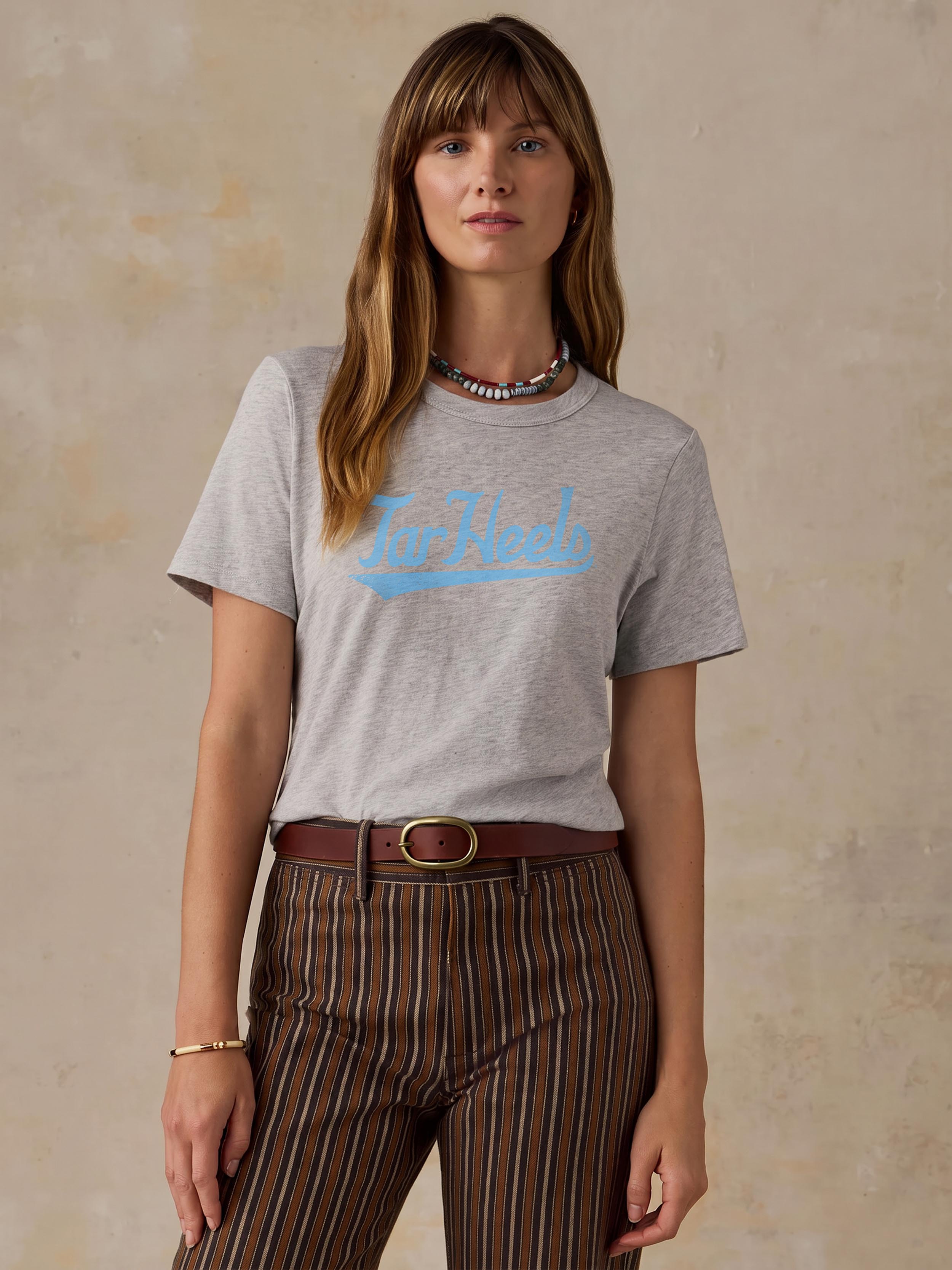 A woman wearing a grey University of North Carolina tee and brown striped pants