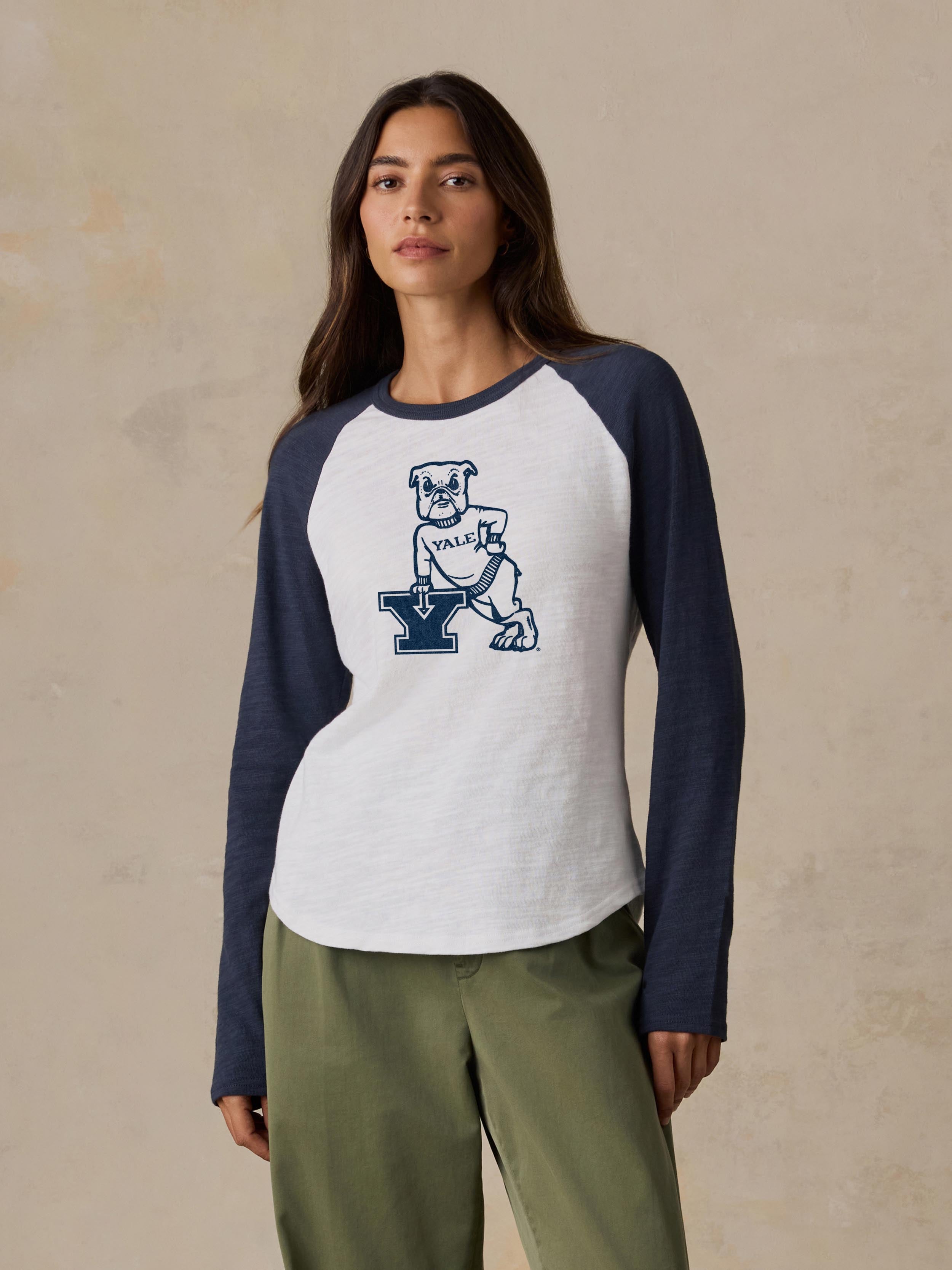 A woman wearing a blue and white Yale baseball tee and green pants