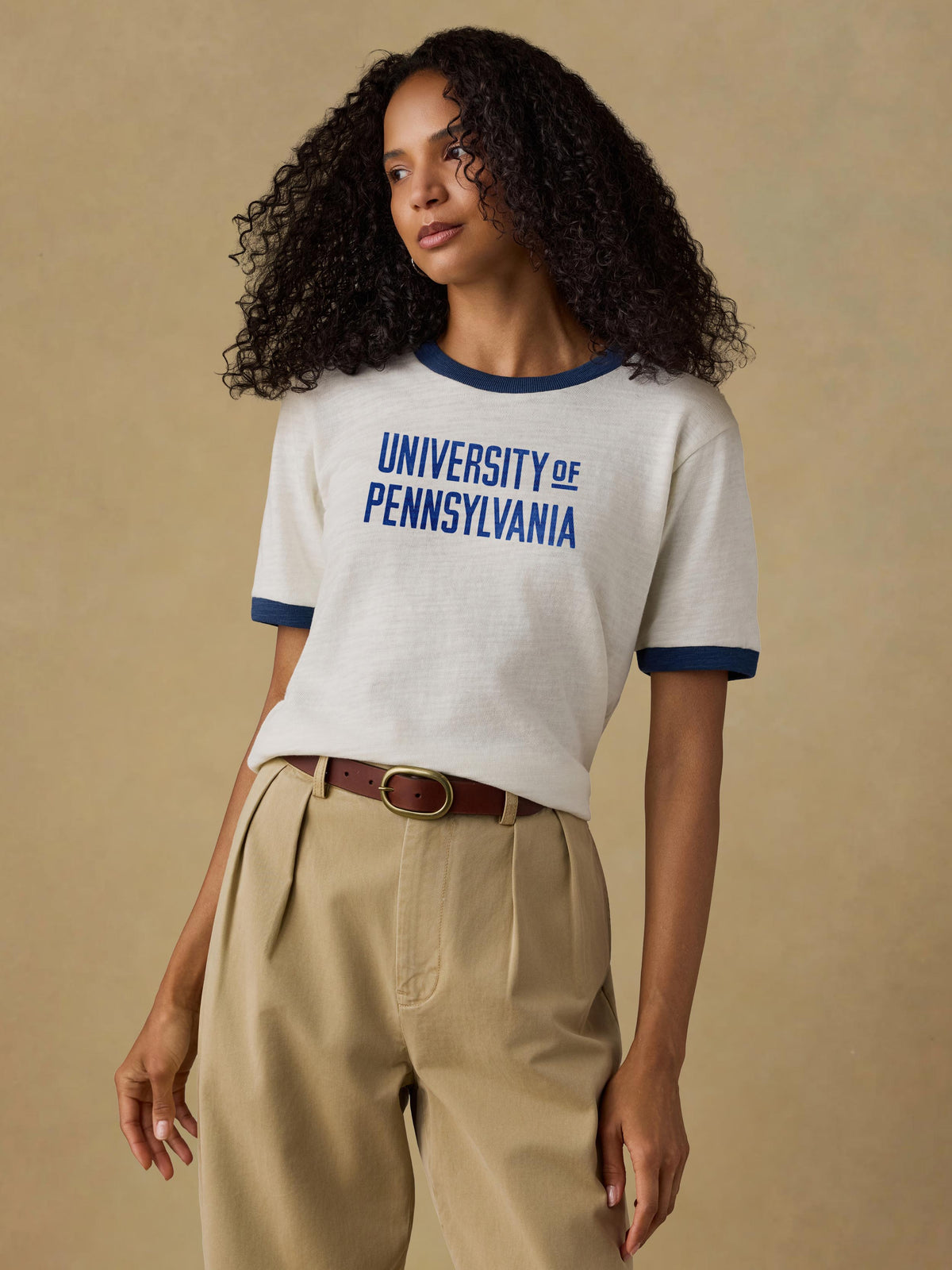 A woman wearing a white University of Pennsylvania tee and beige pants, image 1 of 1