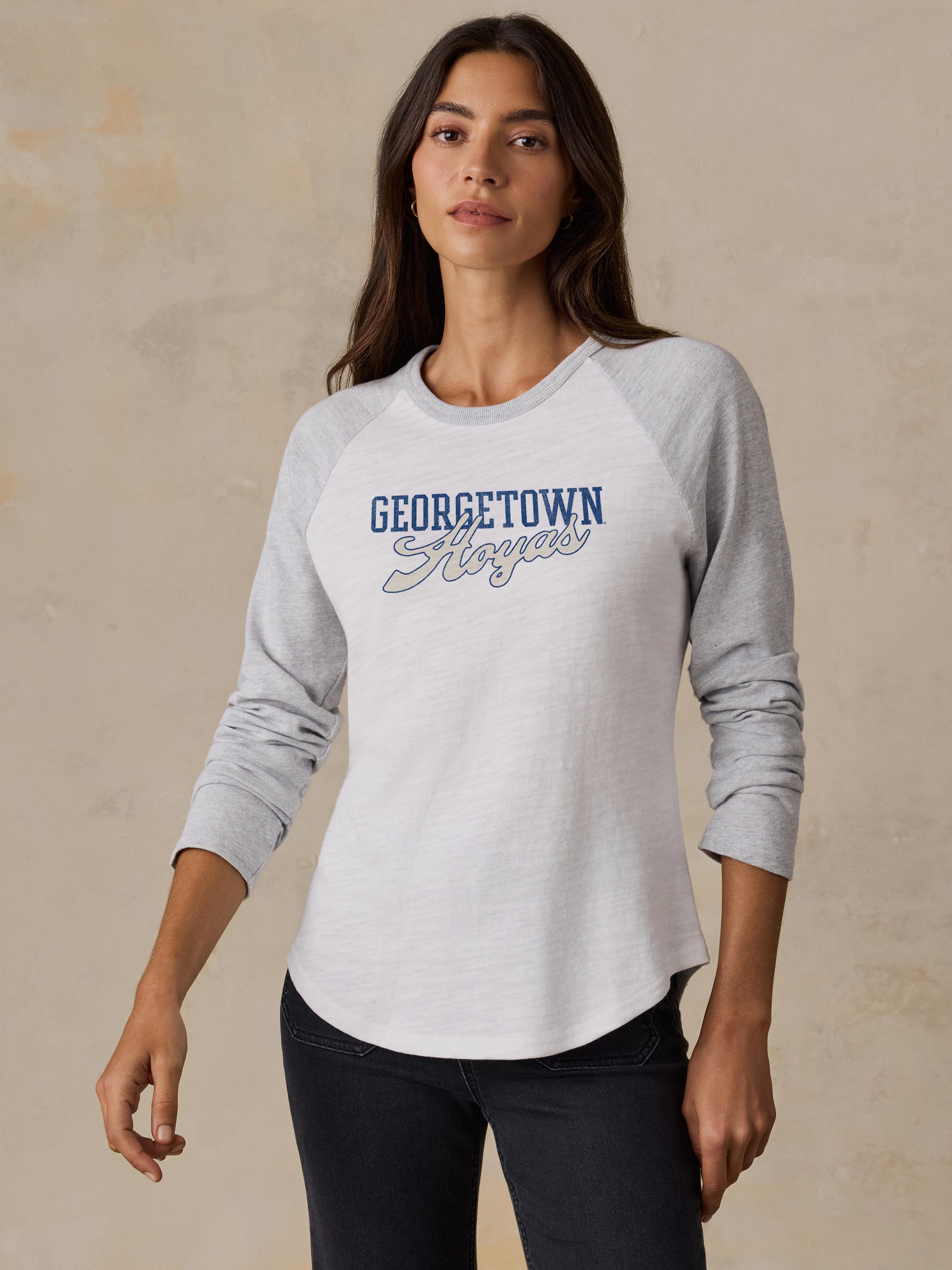 A woman wearing a grey and white Georgetown baseball tee and black jeans