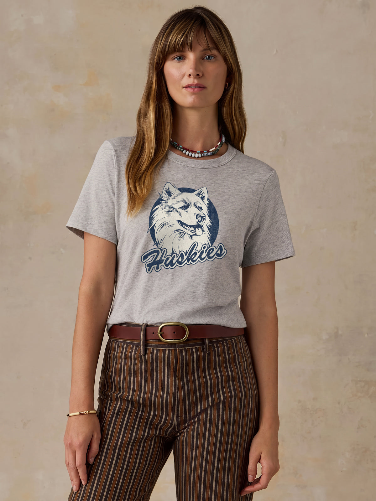 A woman wearing a grey UCONN tee and brown striped shorts, image 1 of 1