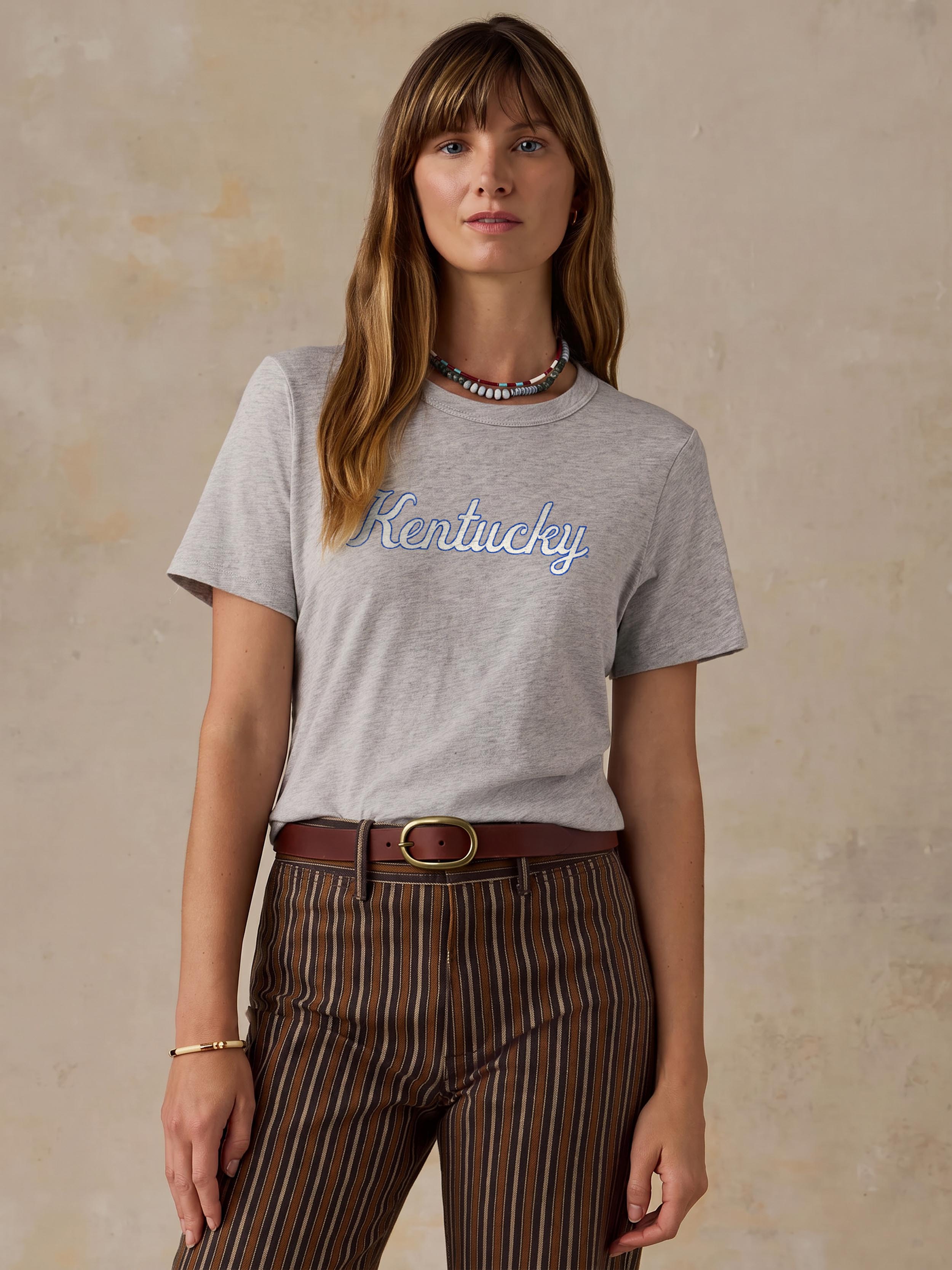 A woman wearing a grey University of Kentucky tee and brown striped pants
