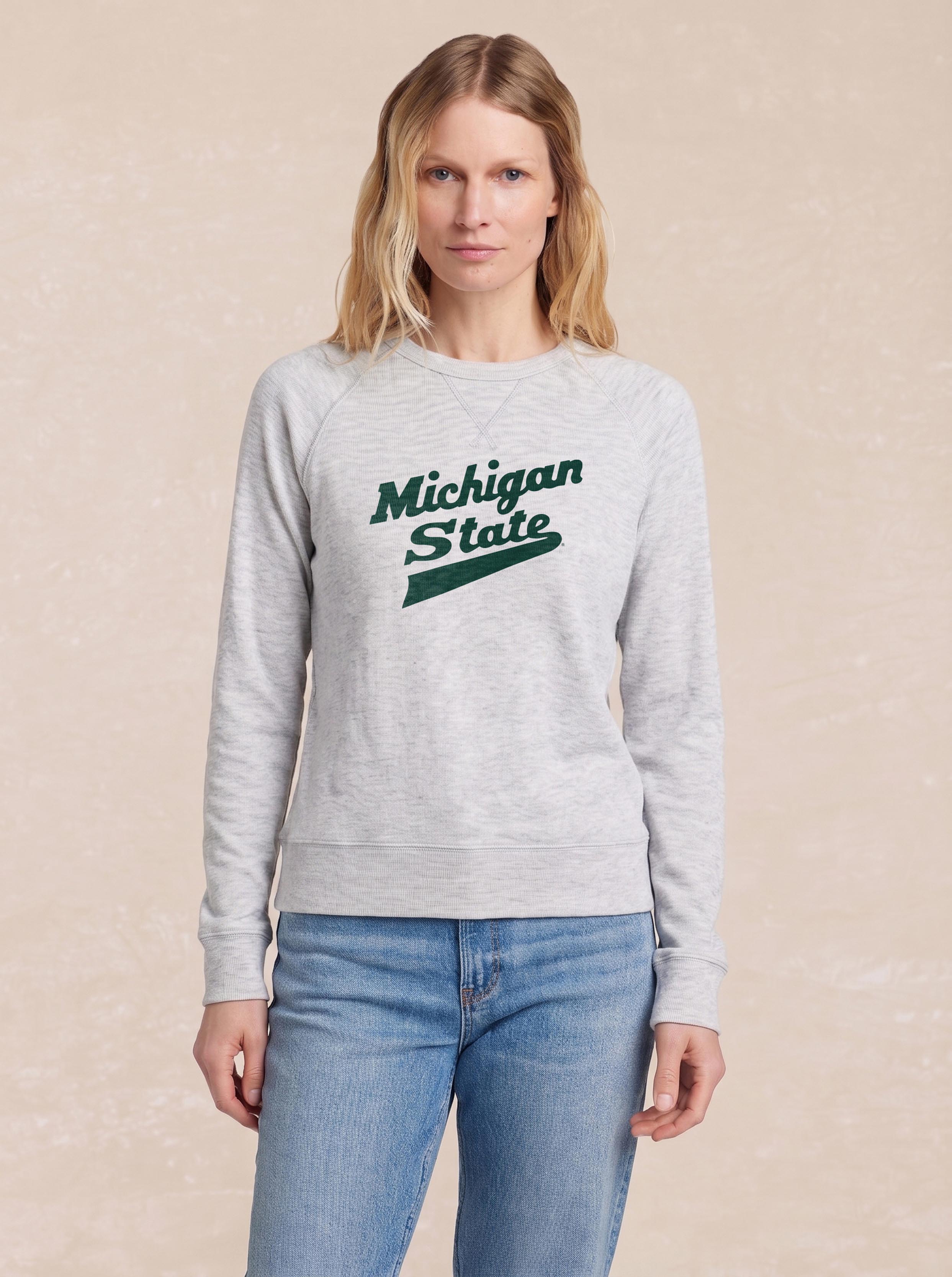 A woman wearing a grey Michigan State crewneck and blue jeans