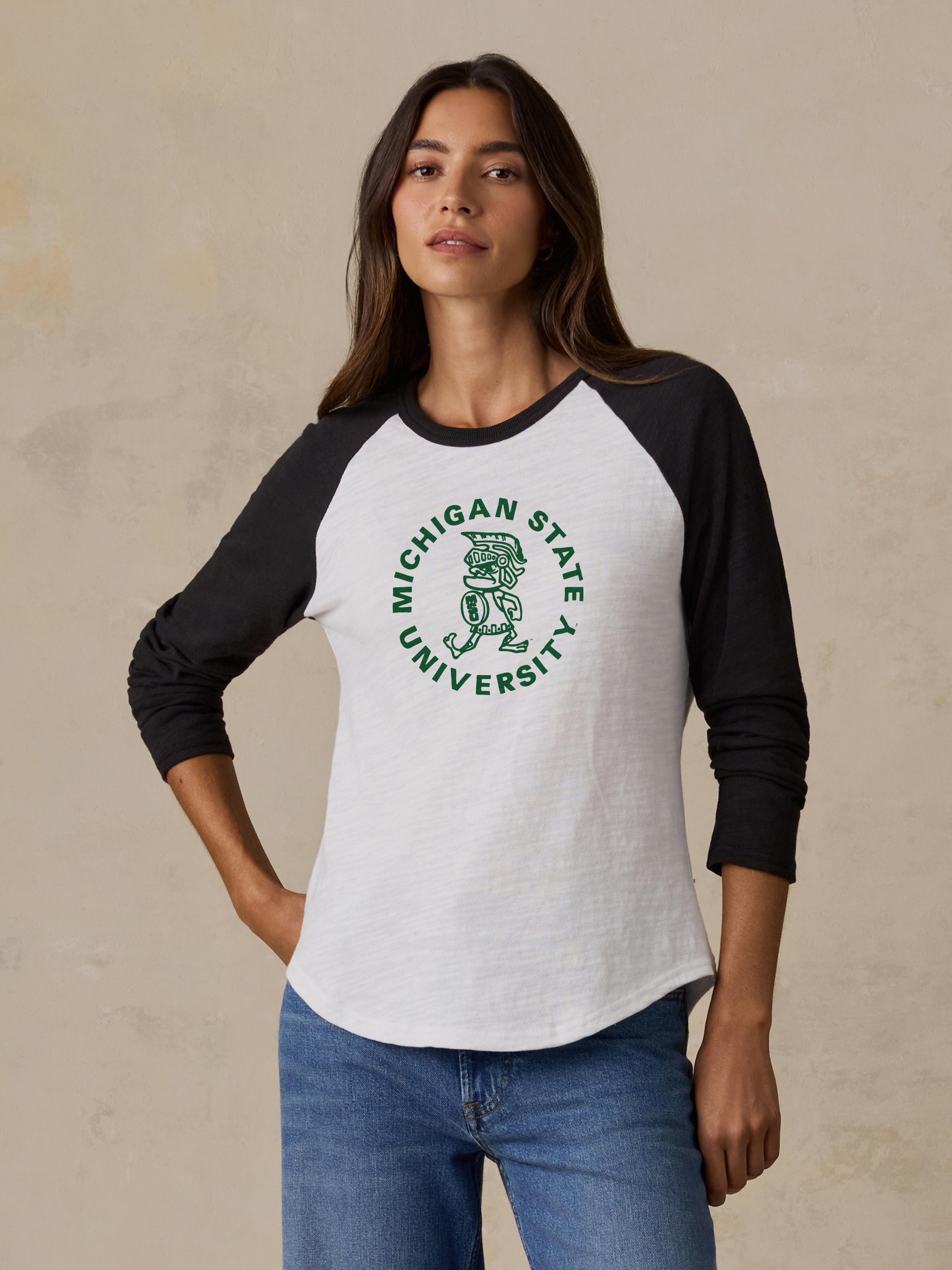A woman is wearing a black and white Michigan State baseball tee and blue jeans