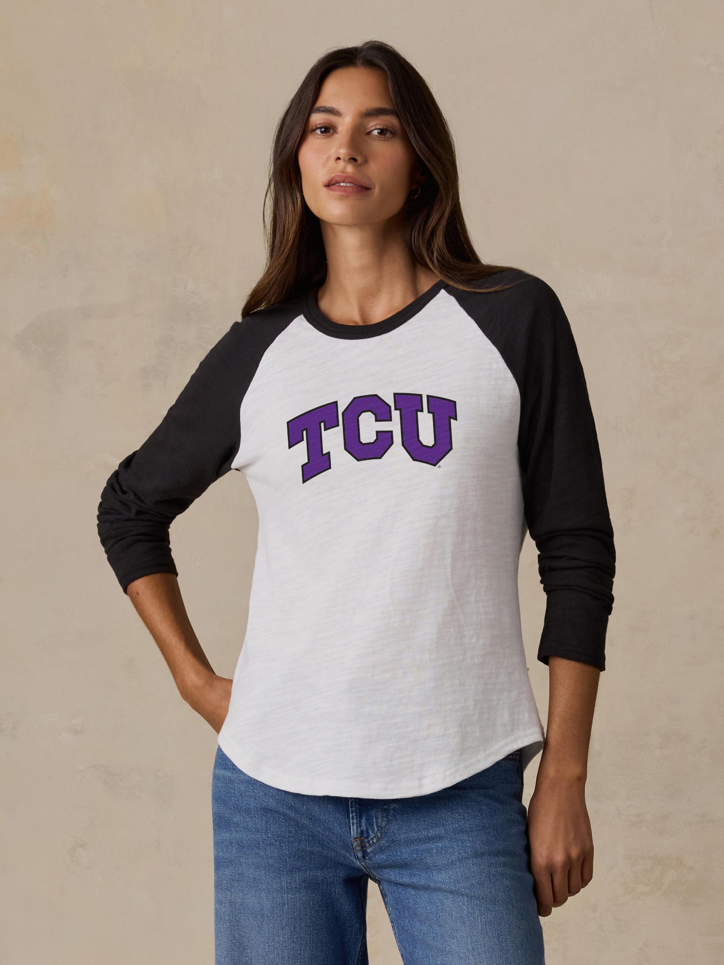A woman wearing a black and white TCU baseball tee and blue jeans