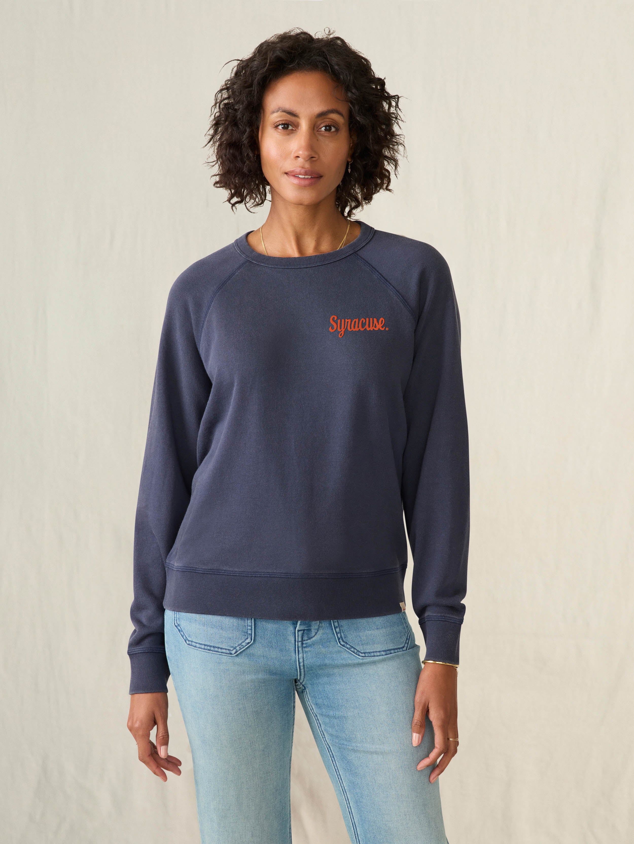 Woman wearing a navy sweatshirt with a Syracuse University graphic on the left chest on a beige background