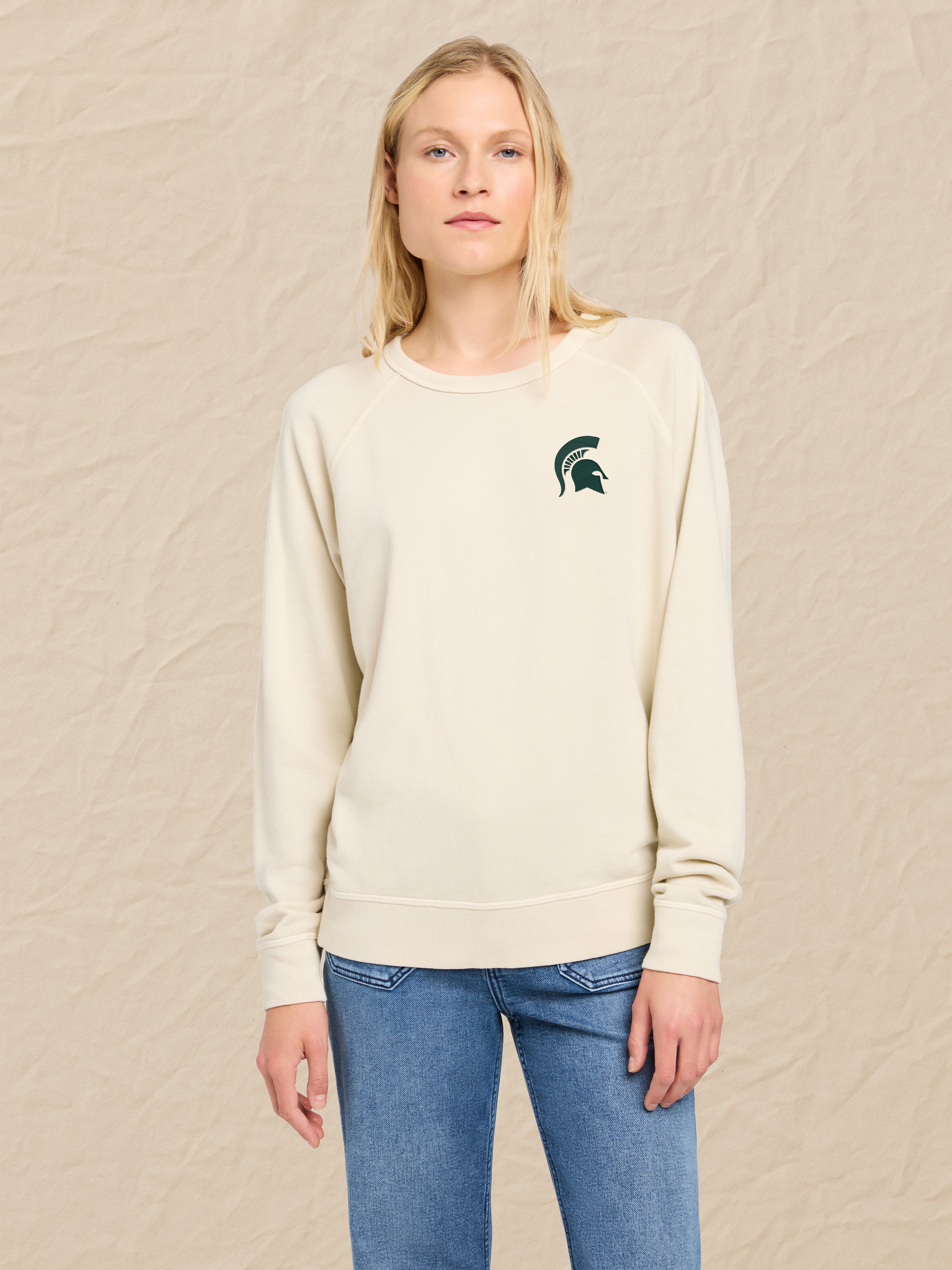 Woman wearing a cream sweatshirt with a Michigan State graphic logo on a beige background