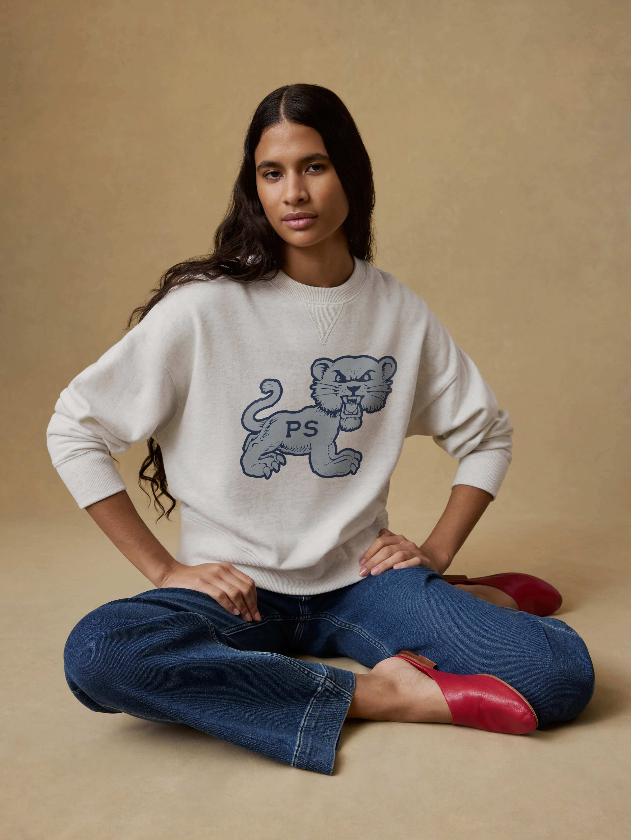 Woman wearing a heather grey crewneck with a Penn State graphic on the center chest against a beige background