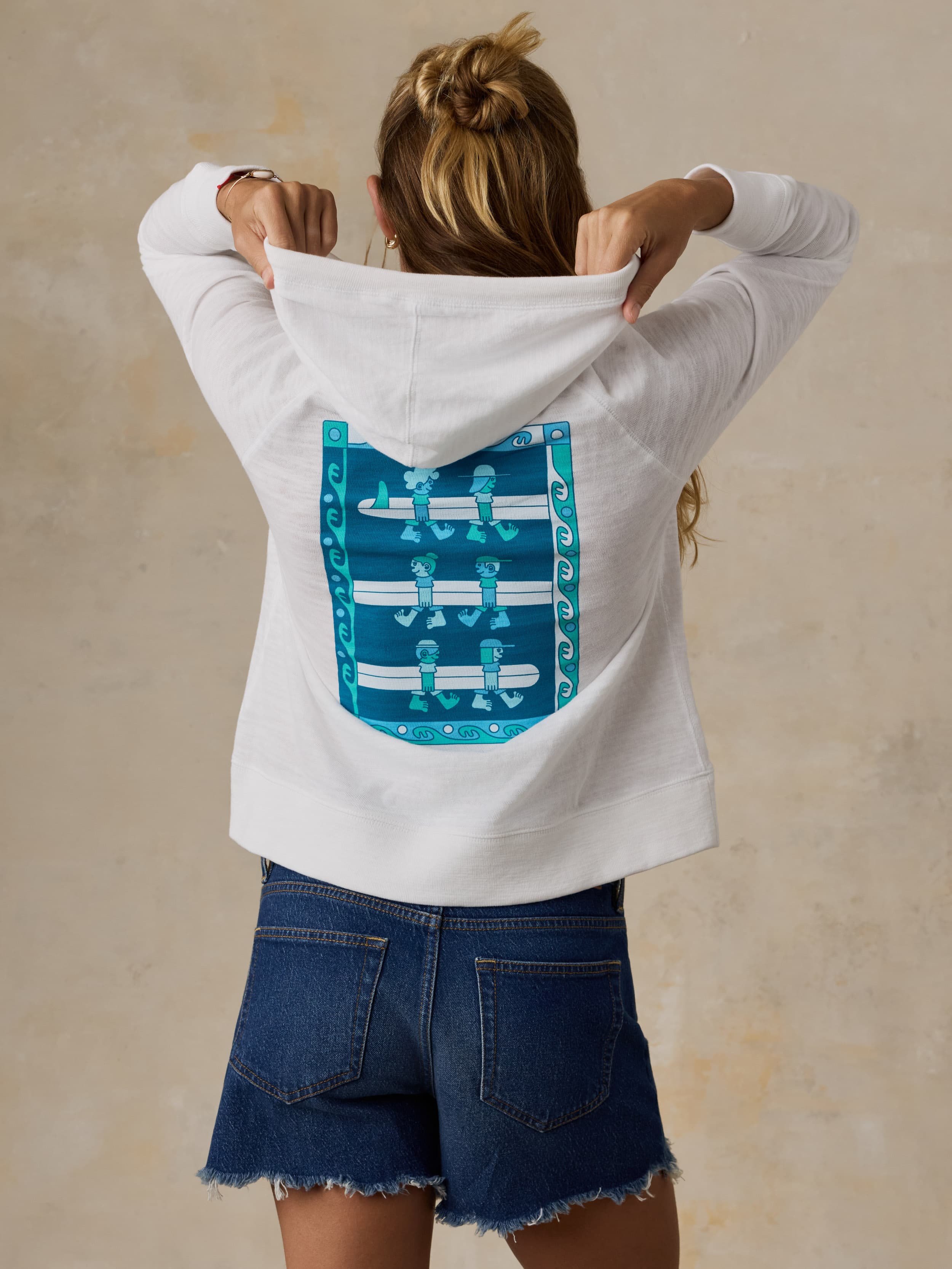 Woman wearing a white Faherty x Surfrider Foundation hoodie against a beige background