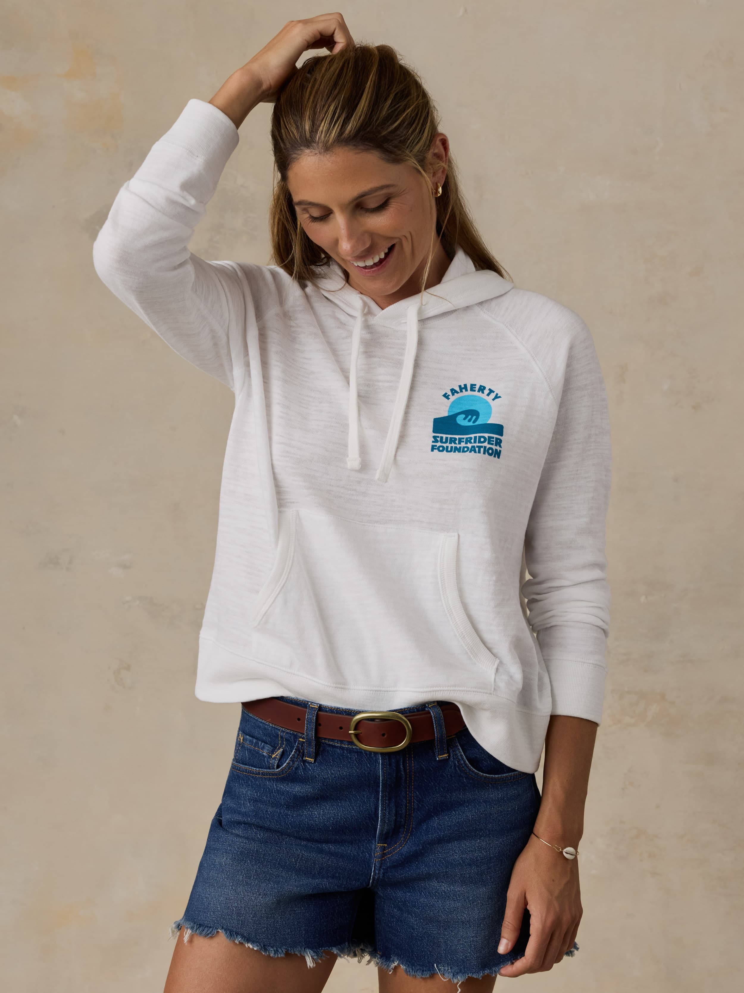 Woman wearing a white Faherty x Surfrider Foundation hoodie against a beige background