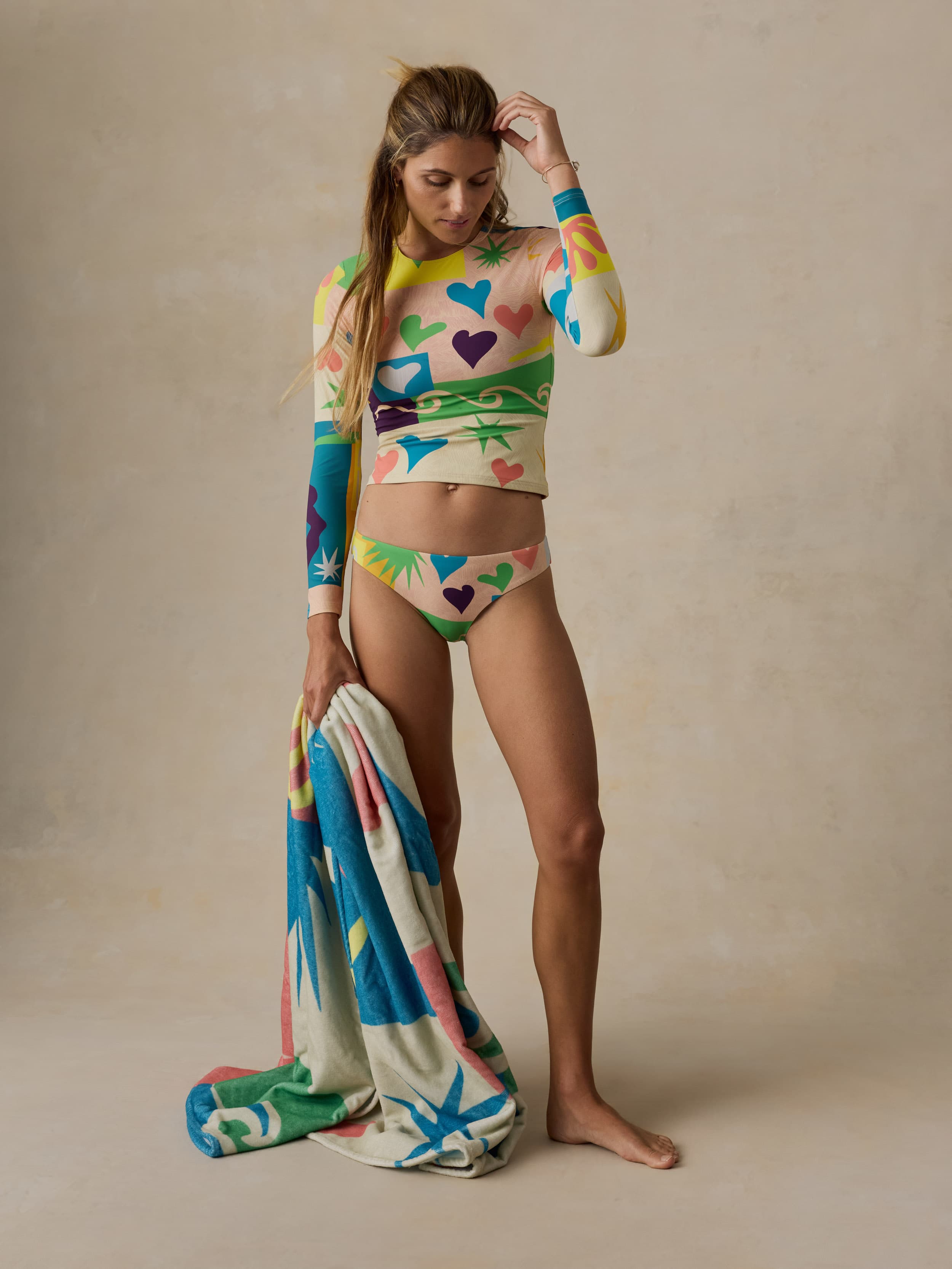 Woman wearing a colorful heart-patterned swimsuit with a matching towel on a beige background