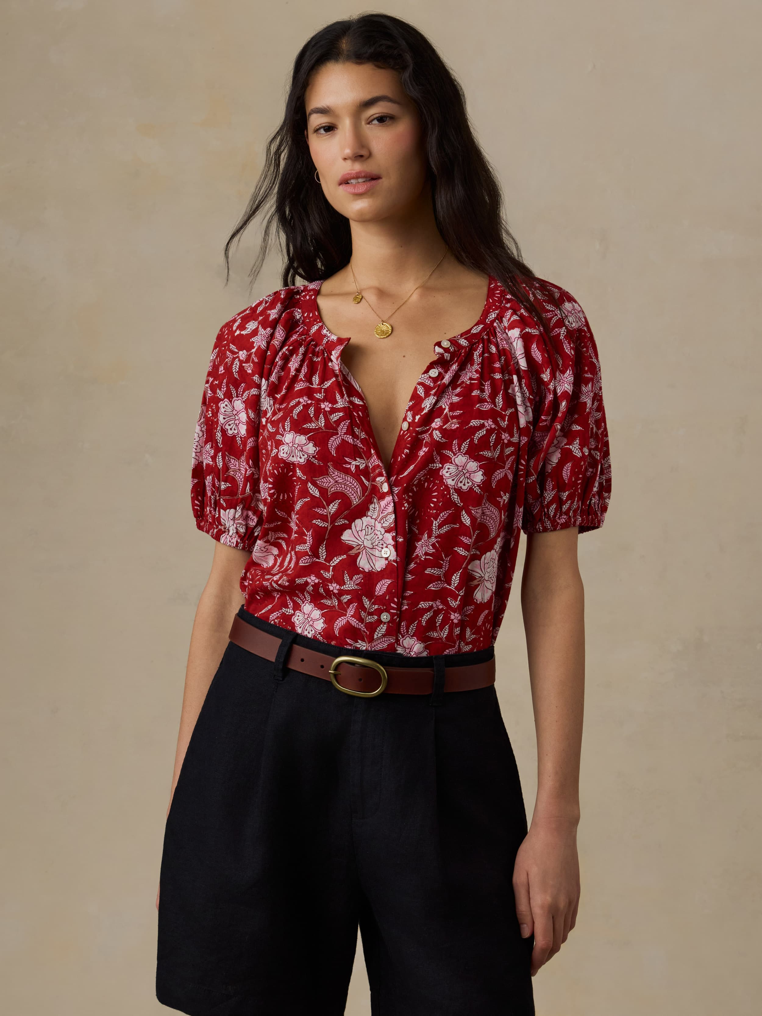 Woman wearing a red floral blouse with black shorts against a beige background