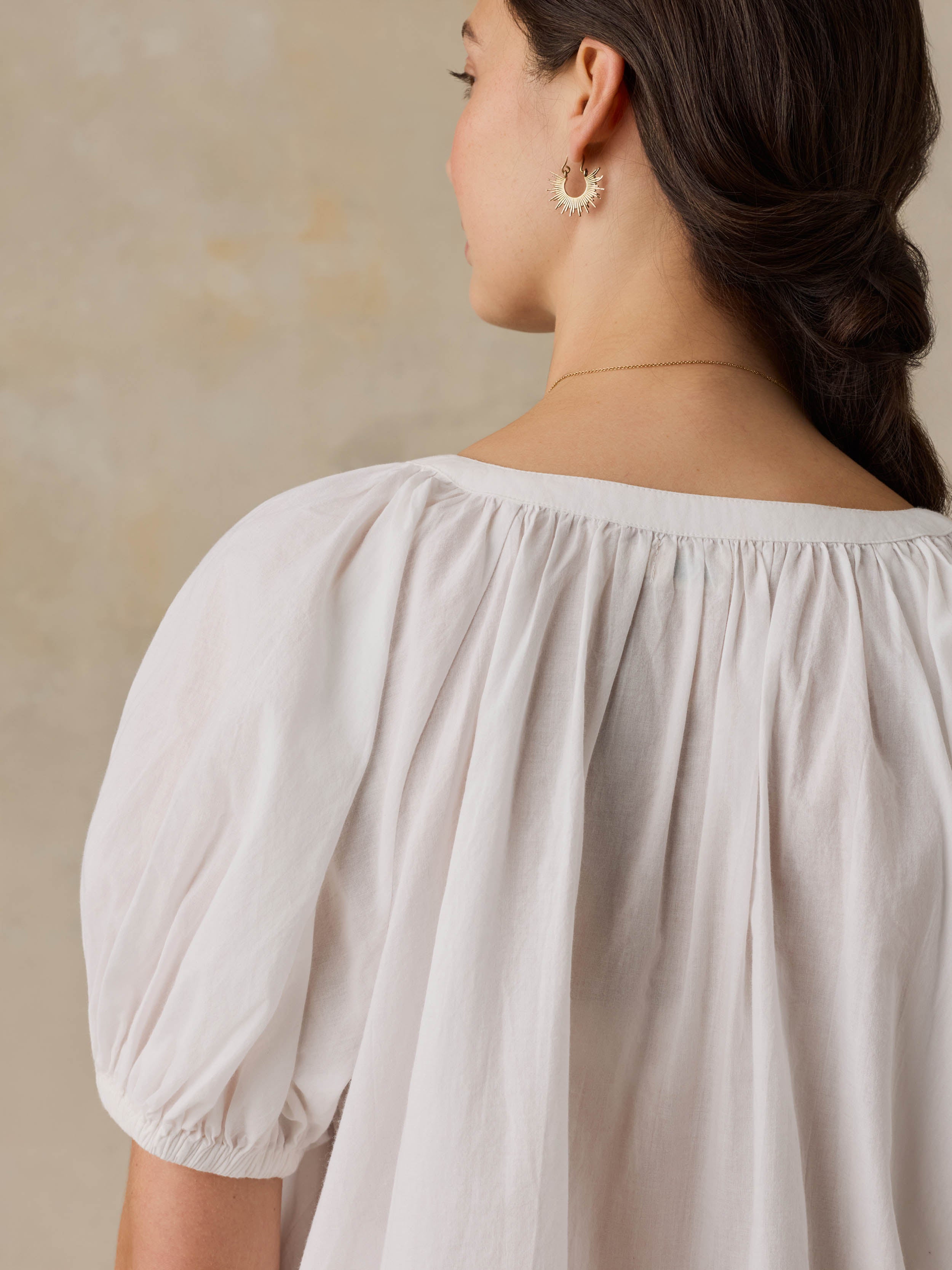 Woman wearing a white blouse with puff sleeves against a beige background