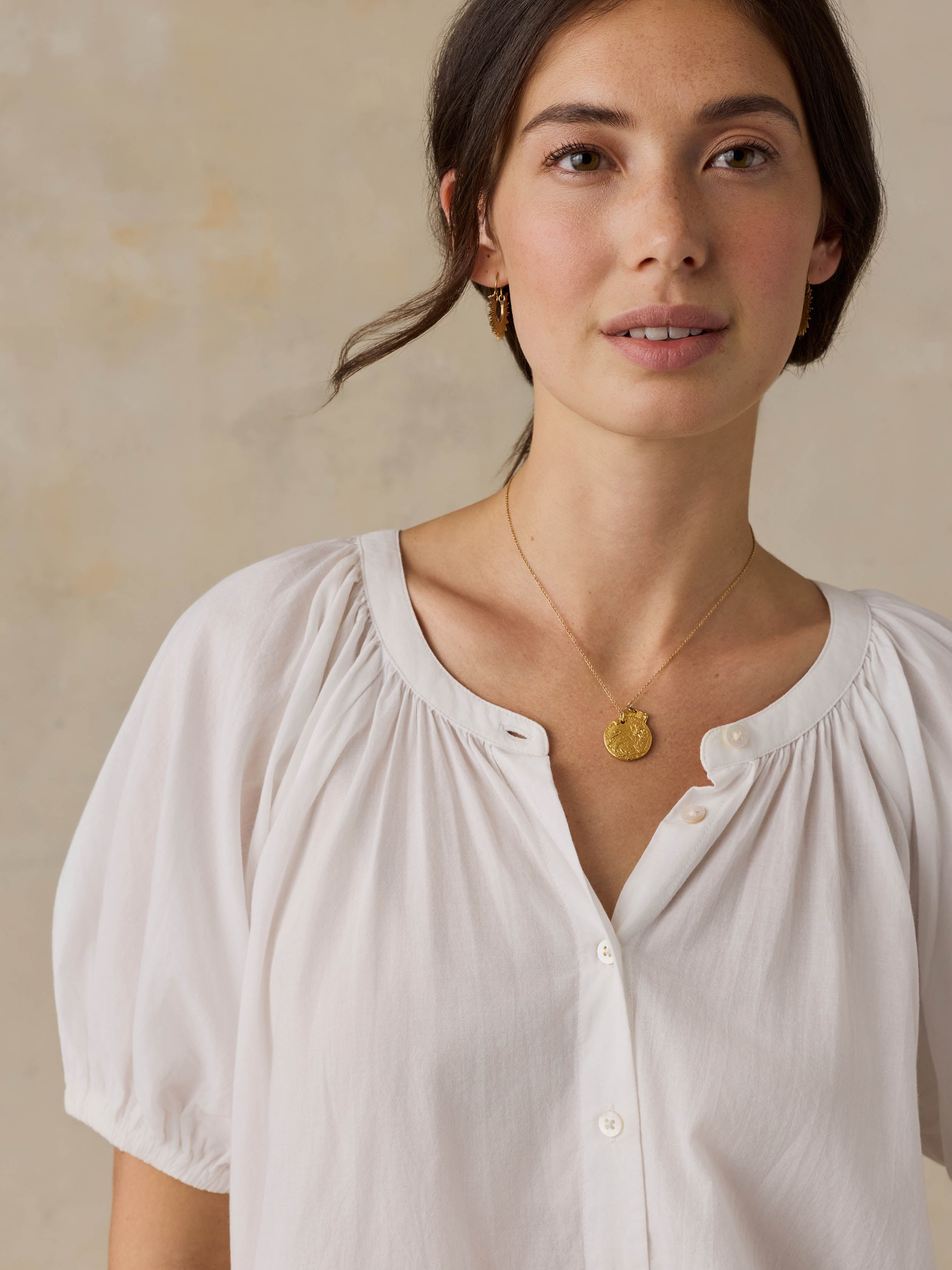 Woman wearing a white blouse with puff sleeves against a beige background