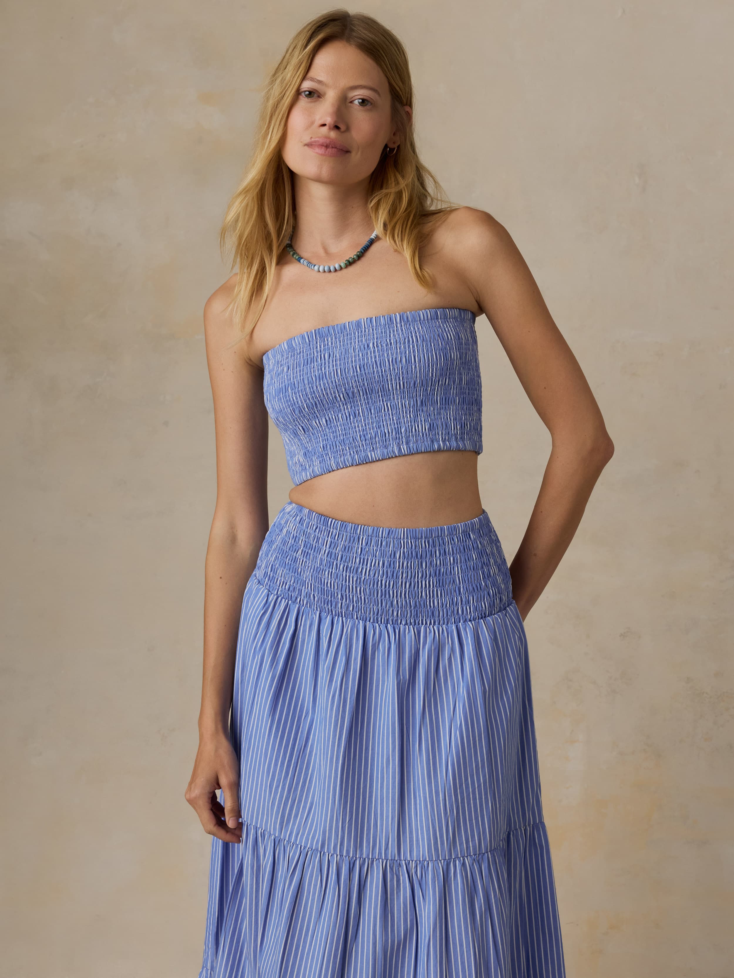 Woman wearing a blue strapless top and skirt set against a beige background