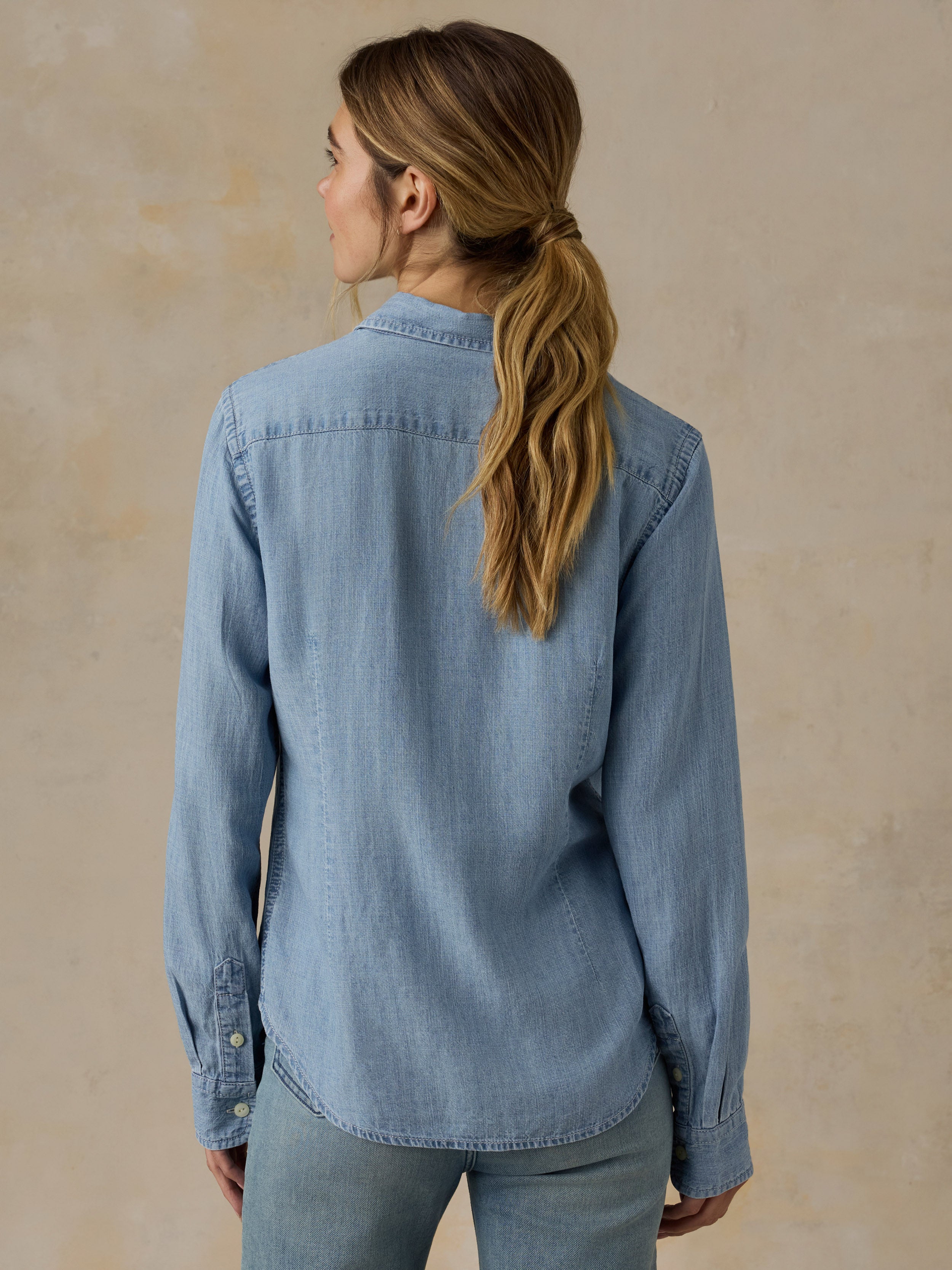 Woman wearing a chambray button down shirt with blue jeans against a beige background