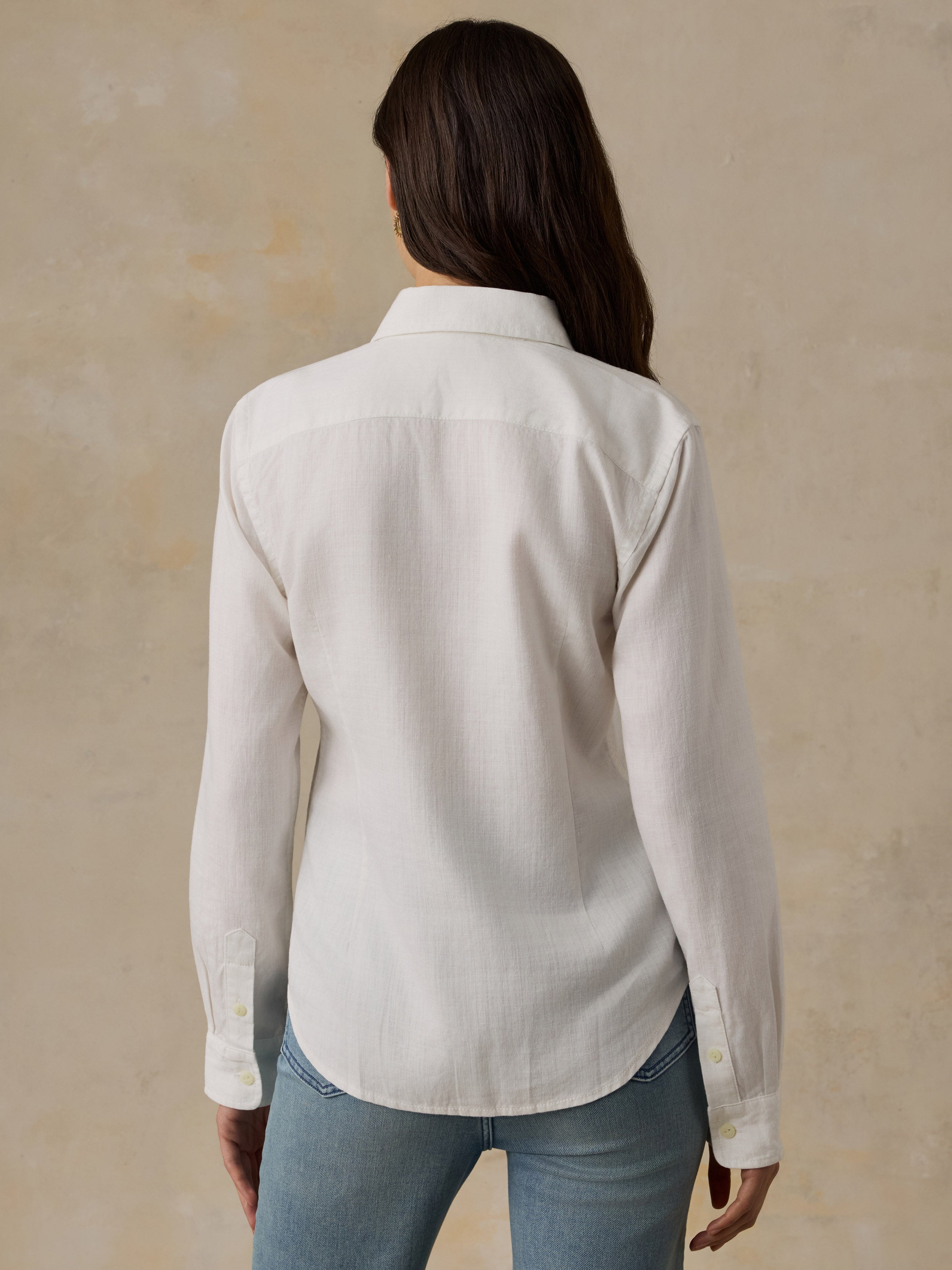 Woman wearing a white chambray button down shirt and blue jeans against a beige background
