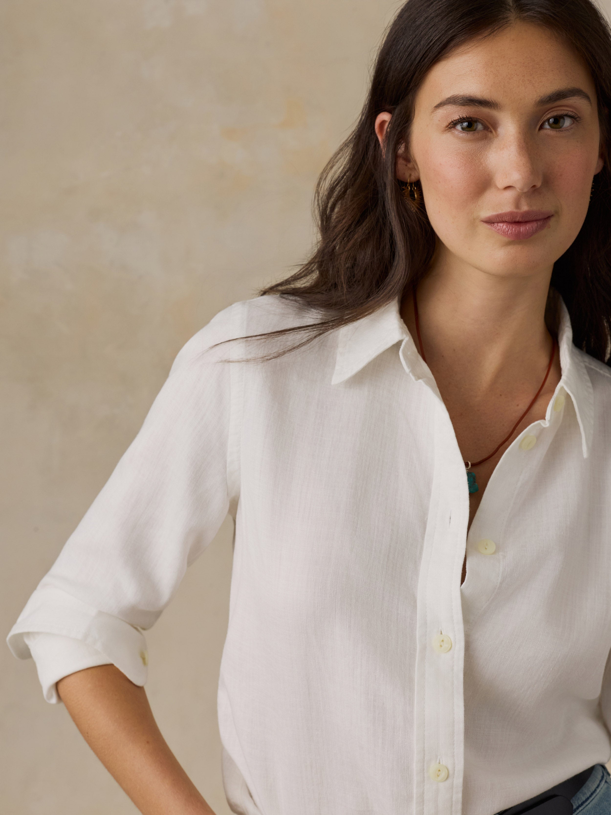 Woman wearing a white chambray button down shirt against a beige background