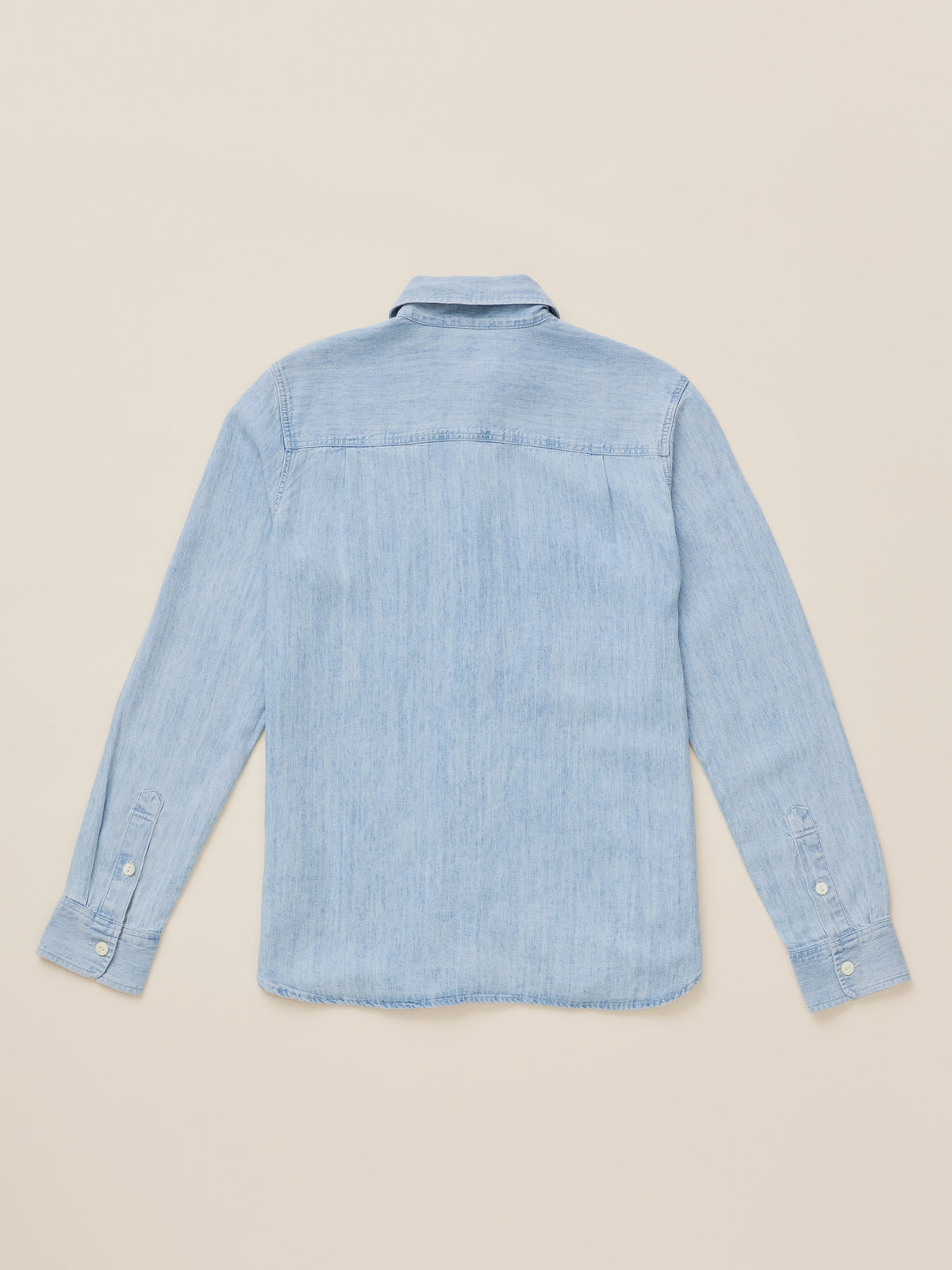 A light blue chambray long-sleeve button-up shirt shown from the back, laid flat on a warm beige background., image 9 of 9