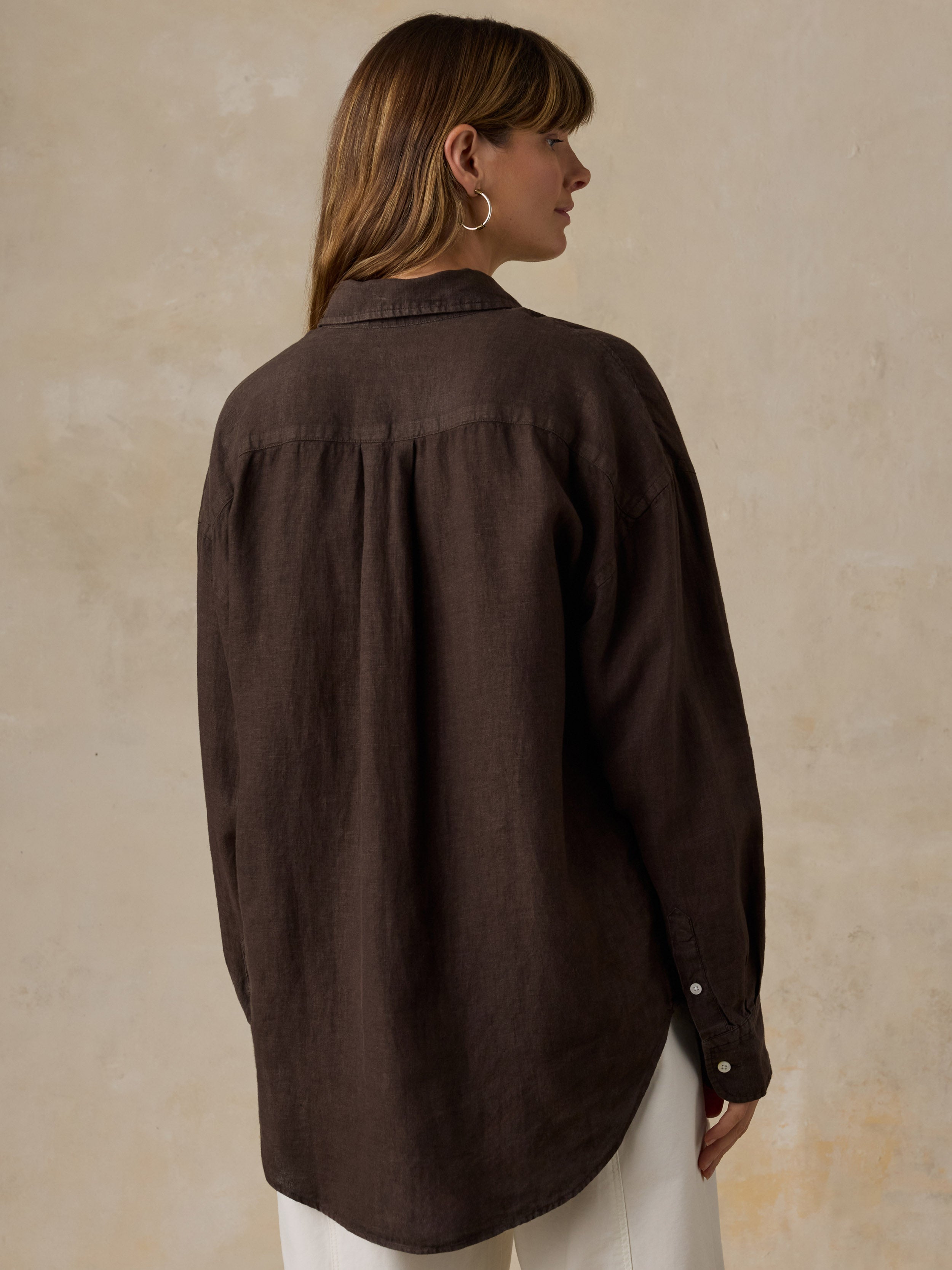 Woman wearing a brown linen shirt with light colored pants against a beige background