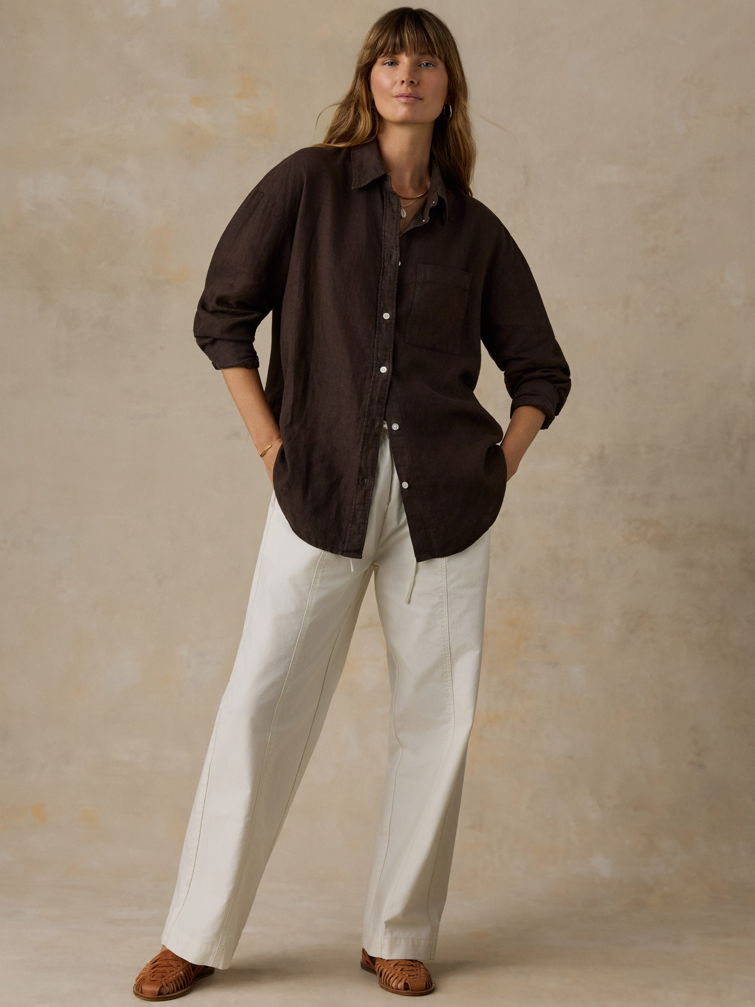 Woman wearing a brown linen shirt with light colored pants against a beige background