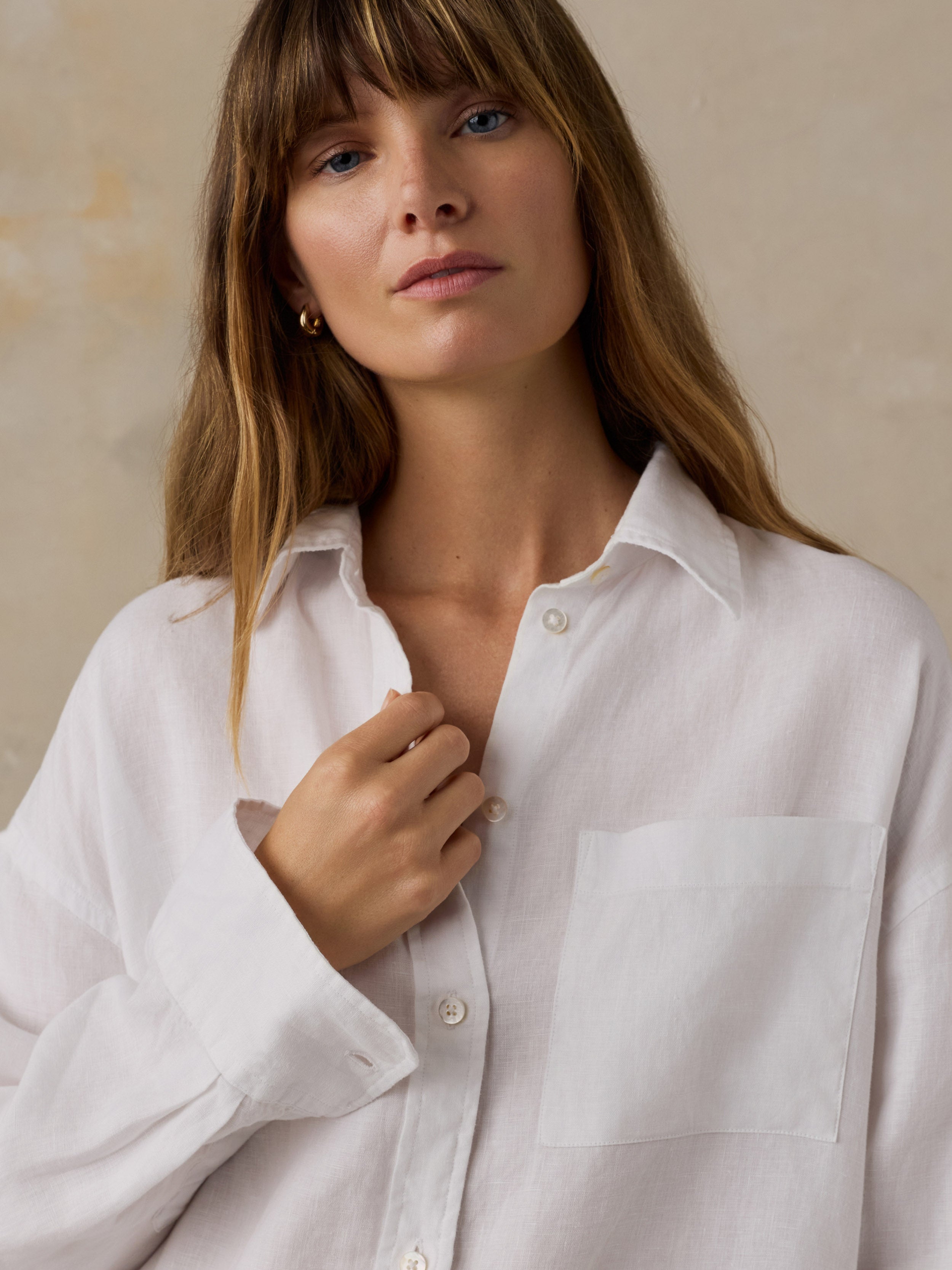Woman wearing a white linen button down shirt against a beige background