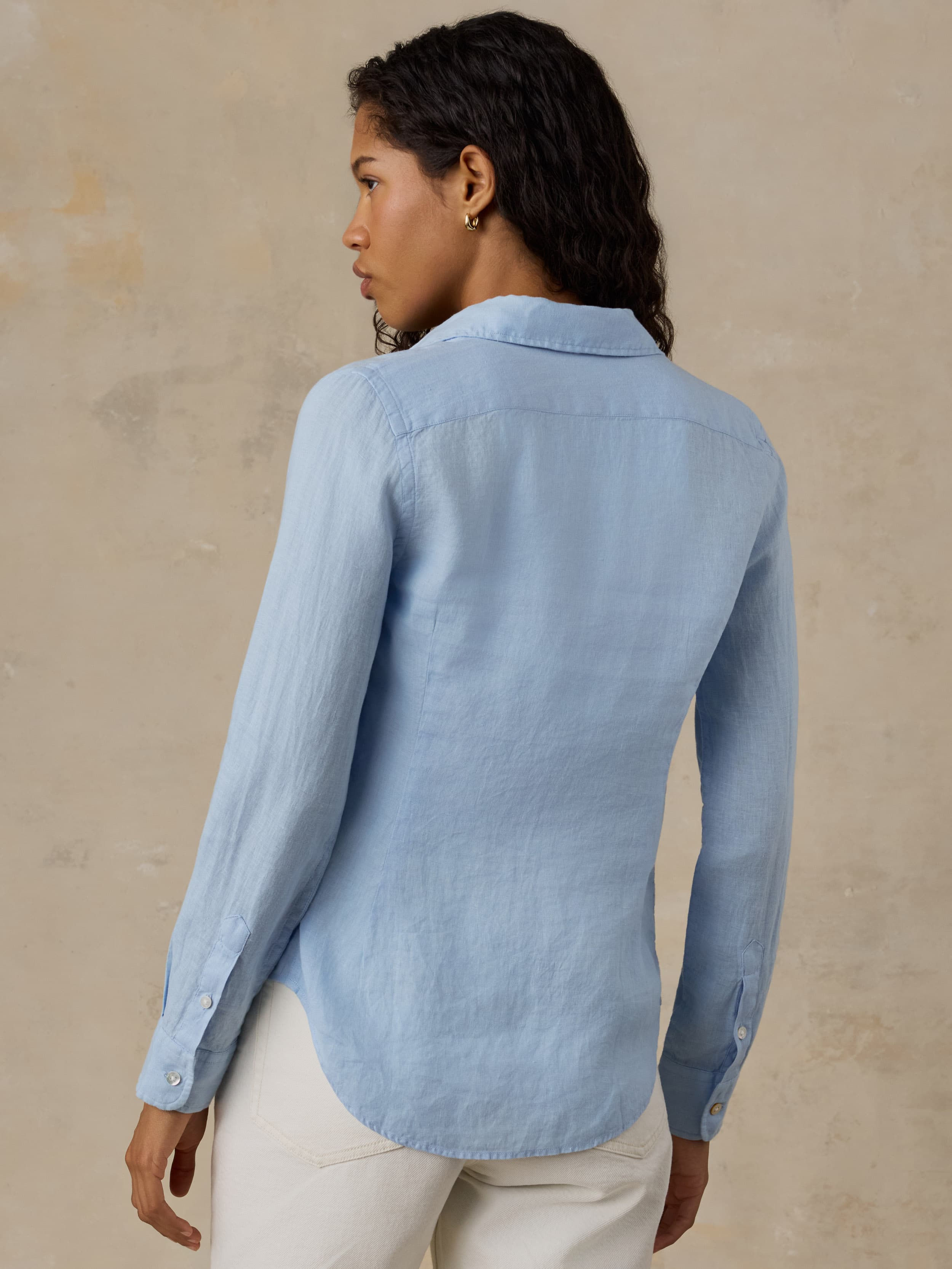 Woman wearing a light blue linen shirt with white pants against a beige background