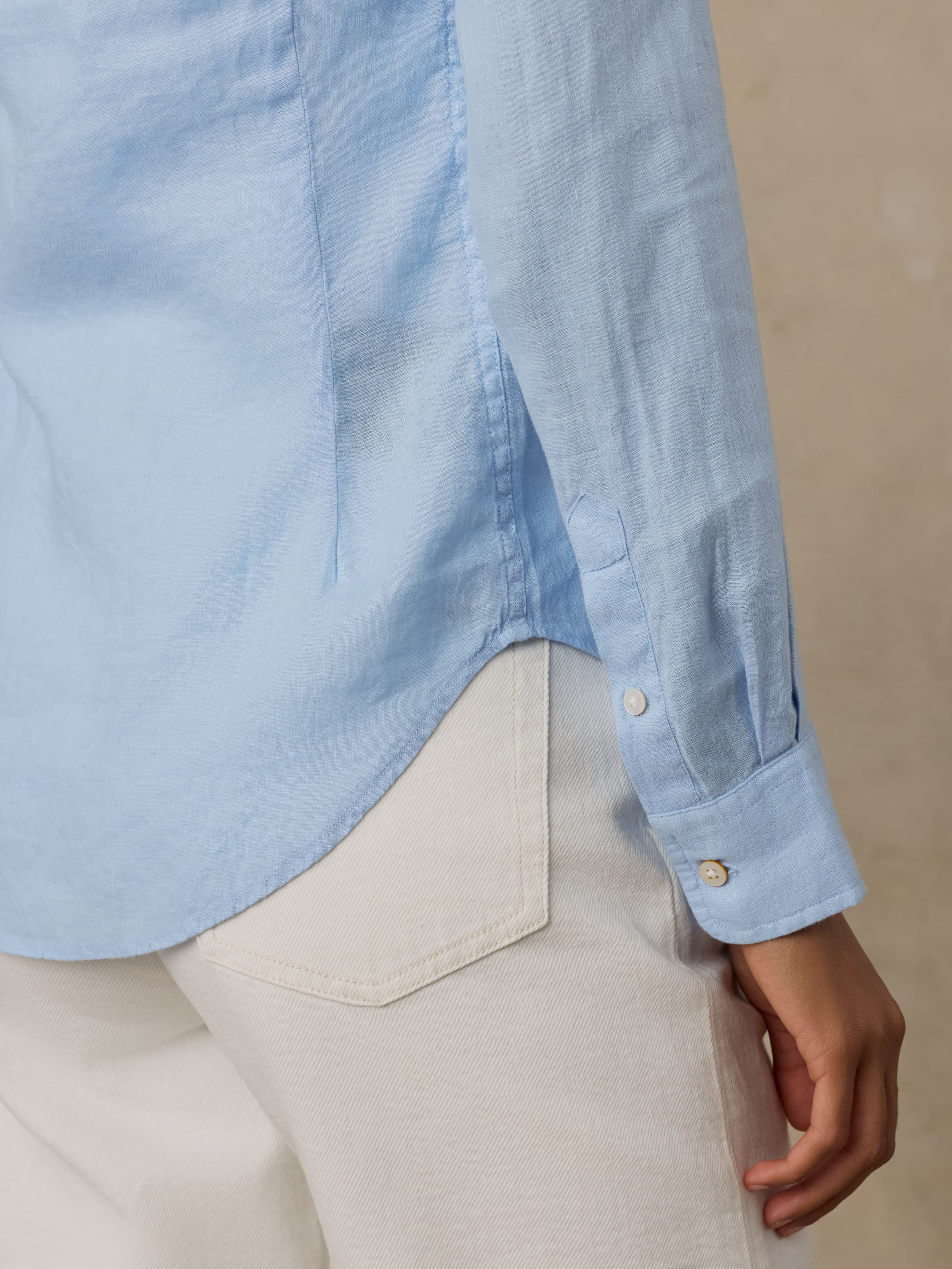 Woman wearing a light blue linen shirt with white pants against a beige background