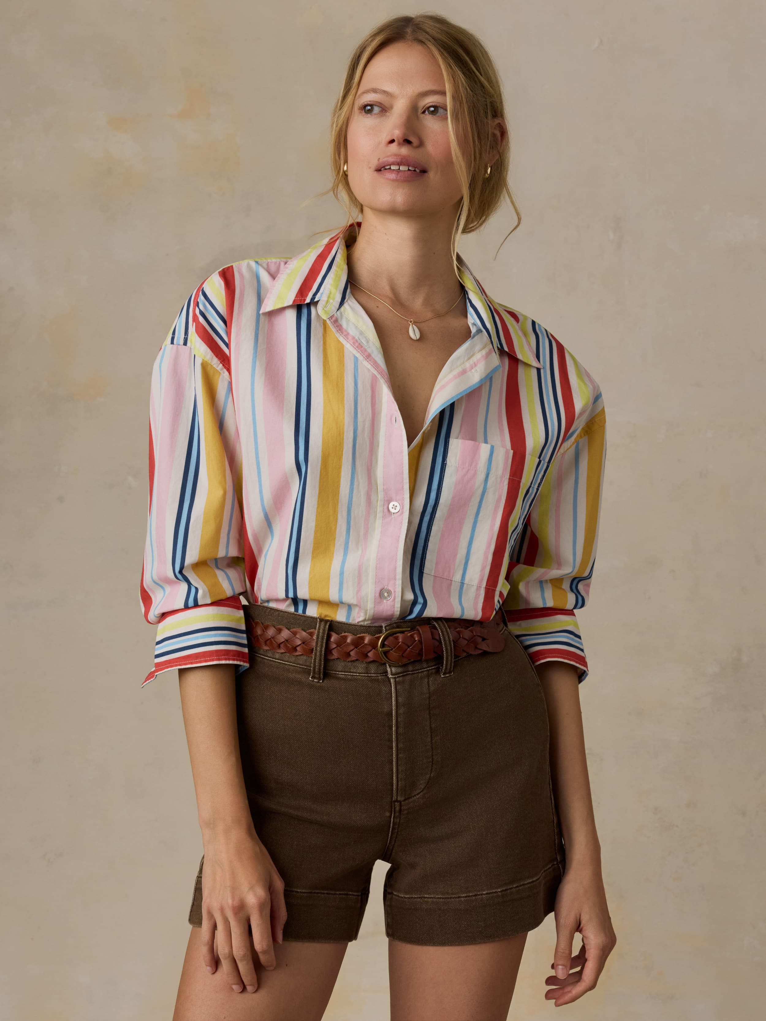 Woman wearing a colorful striped shirt and brown shorts against a beige background